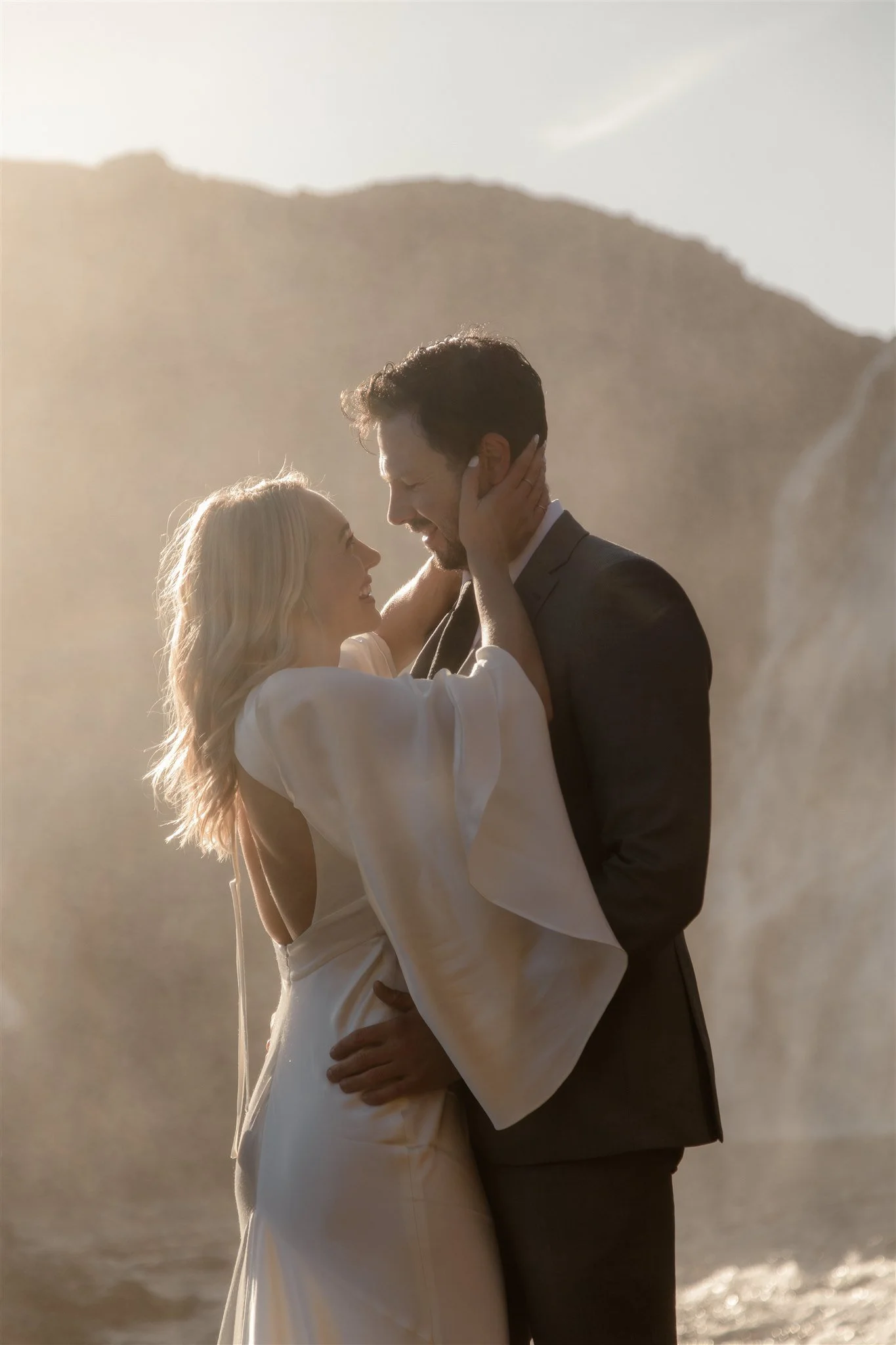 Lord of the Rings Inspired Iceland Engagement Photoshoot at waterfall — couple standing together with Arwen inspired dress with beautiful light and waterfall mist