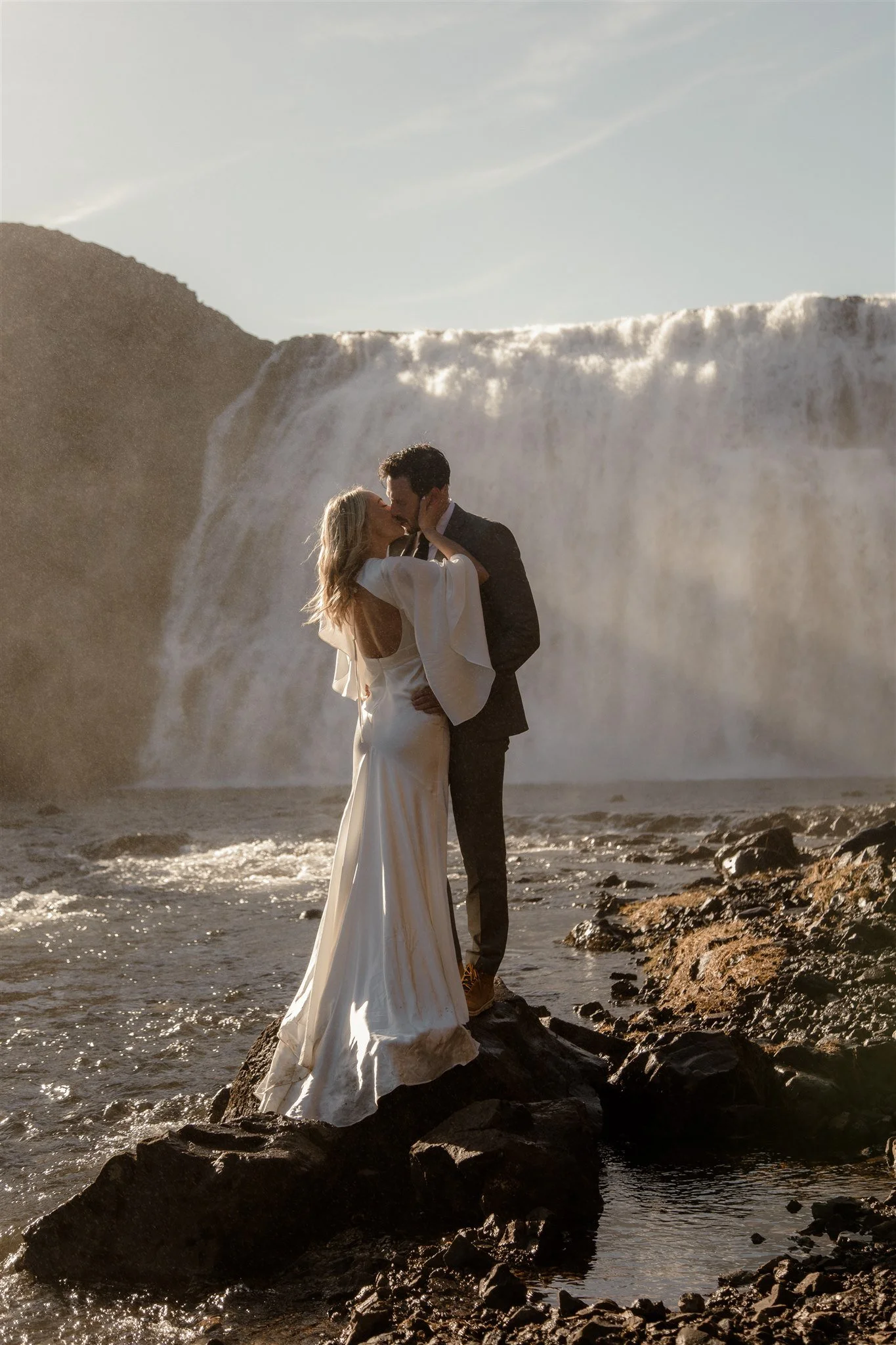 Lord of the Rings Inspired Iceland Engagement Photoshoot at waterfall — couple standing together with Arwen inspired dress with beautiful light and waterfall mist