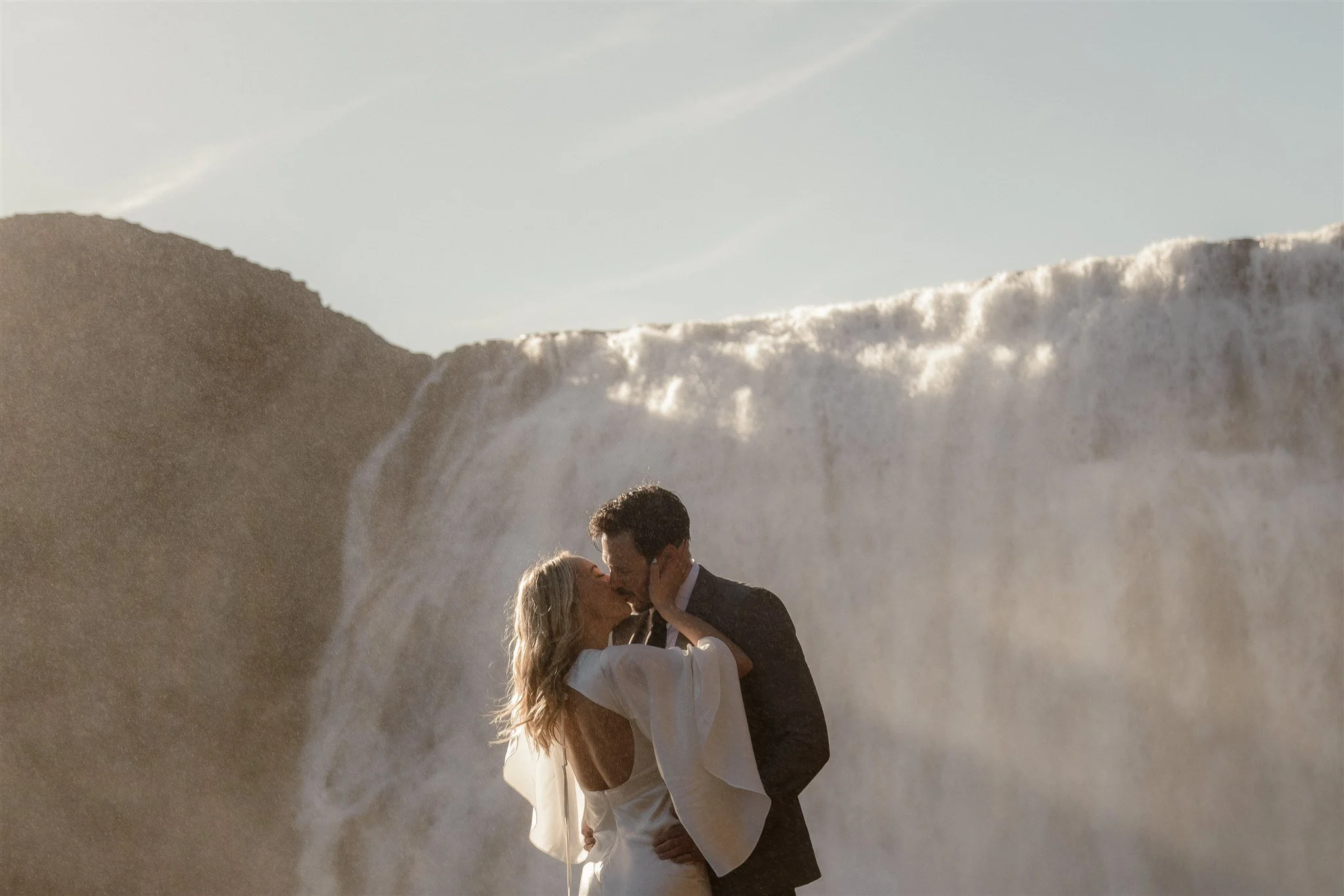 Lord of the Rings Inspired Iceland Engagement Photoshoot at waterfall — couple standing together with Arwen inspired dress with beautiful light and waterfall mist