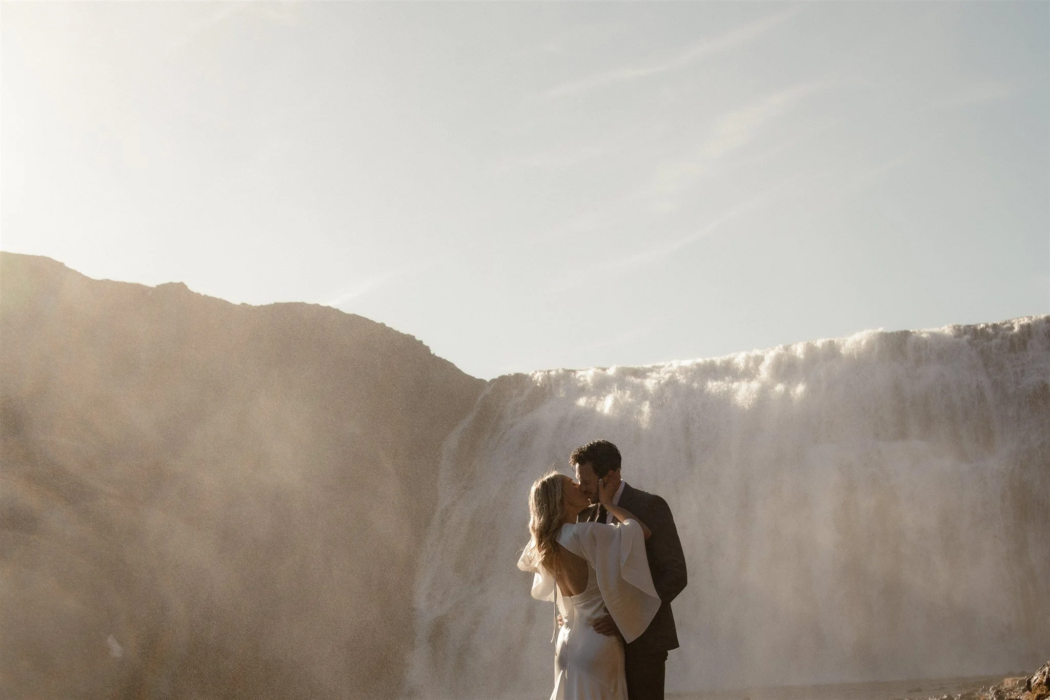Lord of the Rings Inspired Iceland Engagement Photoshoot at waterfall — couple standing together with Arwen inspired dress with beautiful light and waterfall mist