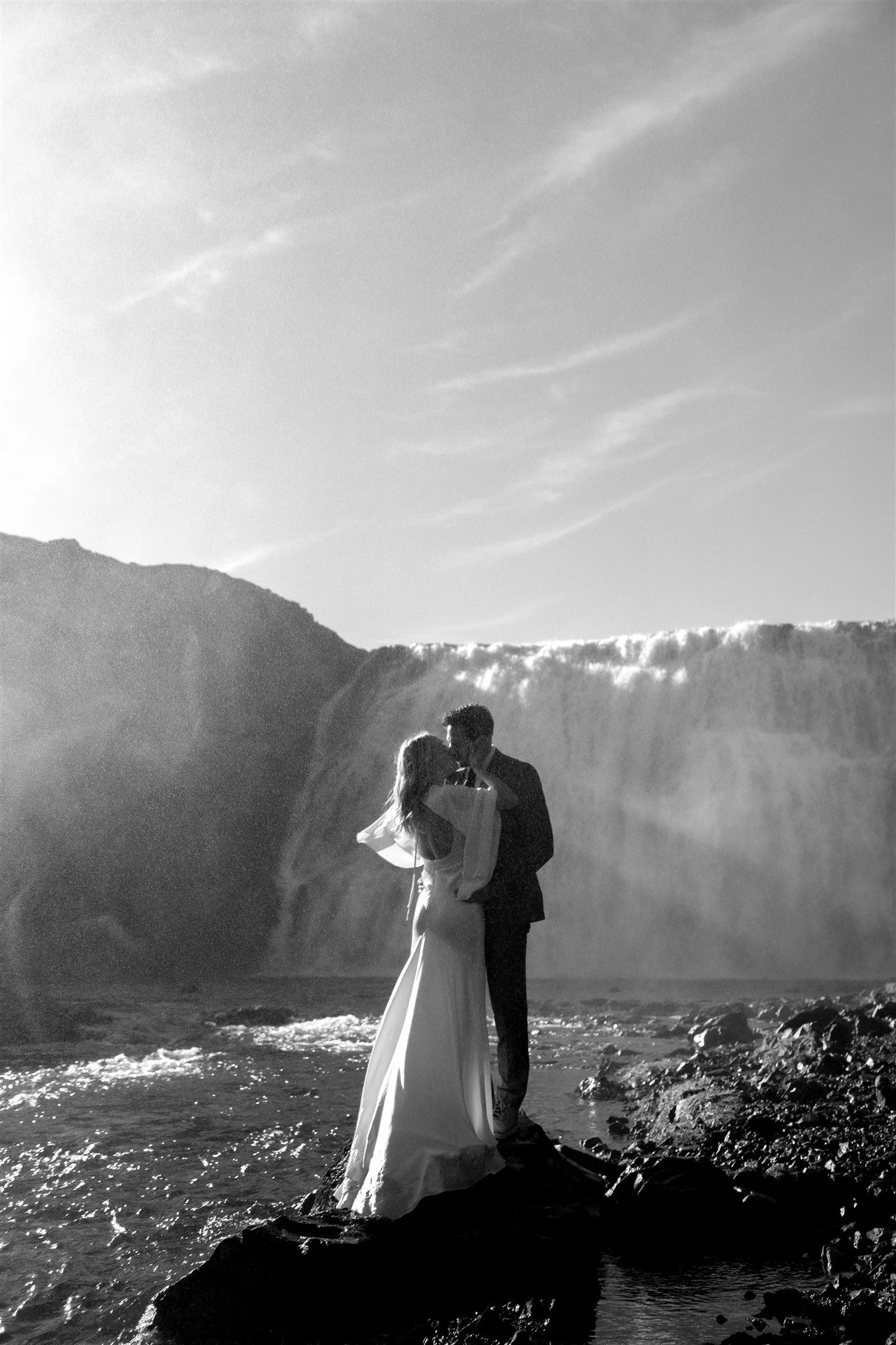 Lord of the Rings Inspired Iceland Engagement Photoshoot at waterfall — couple standing together with Arwen inspired dress with beautiful light and waterfall mist