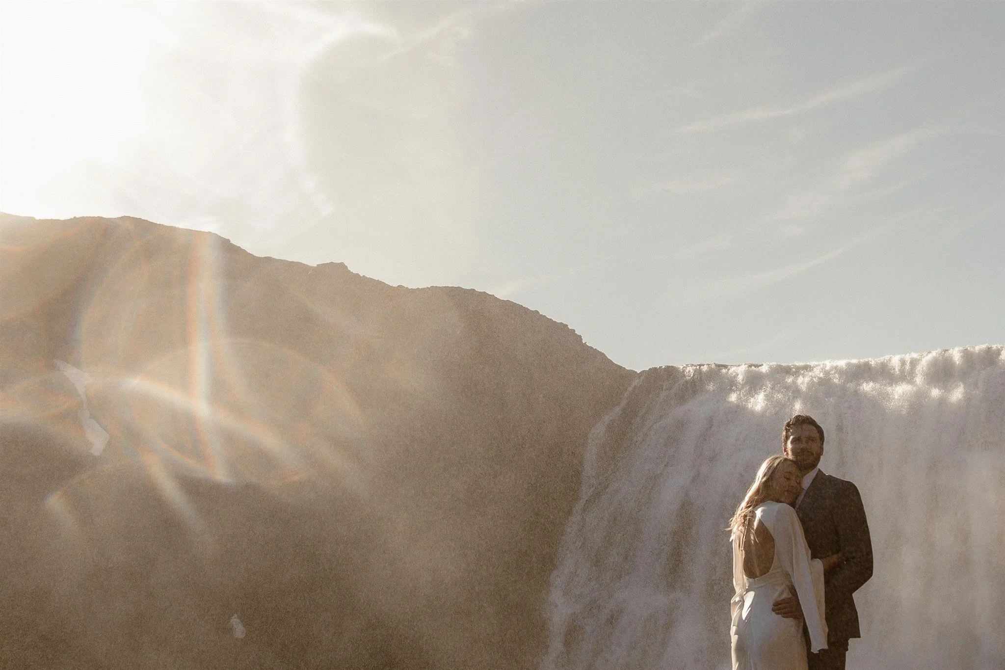 Lord of the Rings Inspired Iceland Engagement Photoshoot at waterfall — couple standing together with Arwen inspired dress with beautiful light and waterfall mist