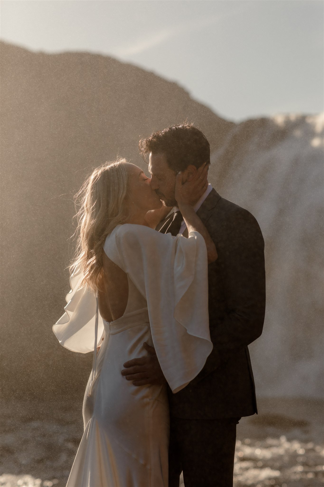 Lord of the Rings Inspired Iceland Engagement Photoshoot at waterfall — couple standing together with Arwen inspired dress with beautiful light and waterfall mist