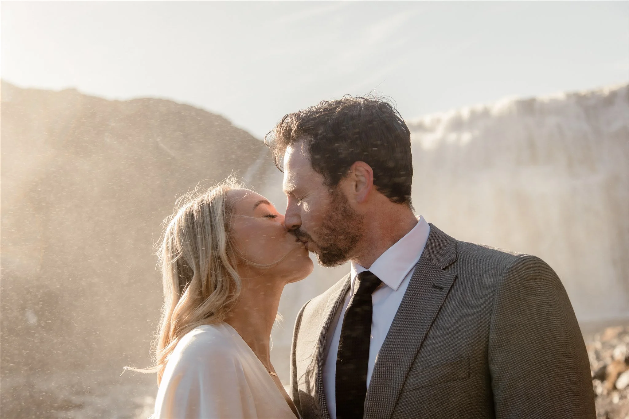 Lord of the Rings Inspired Iceland Engagement Photoshoot at waterfall — couple standing together with Arwen inspired dress with beautiful light and waterfall mist