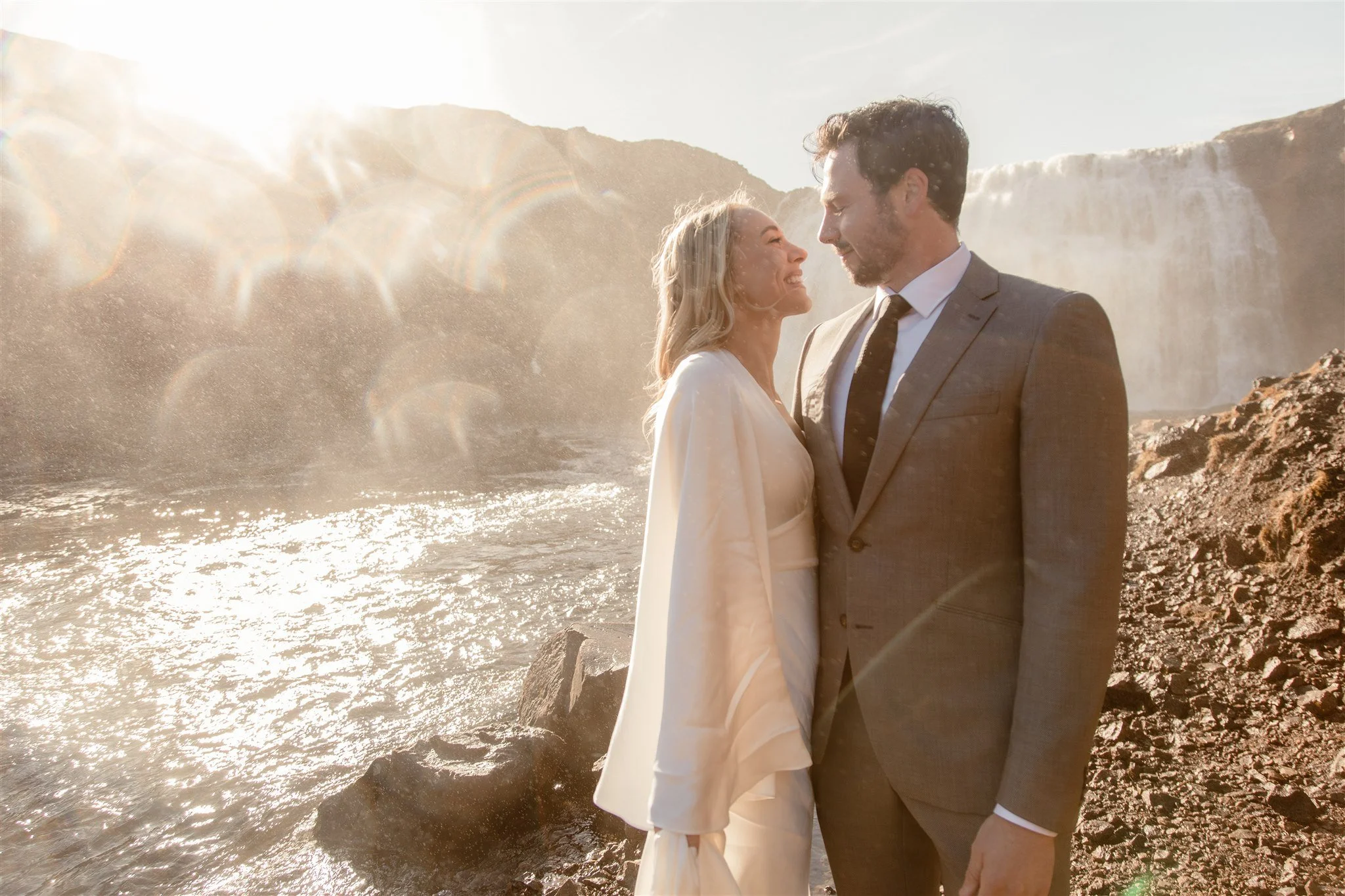 Lord of the Rings Inspired Iceland Engagement Photoshoot at waterfall — couple standing together with Arwen inspired dress with beautiful light and waterfall mist