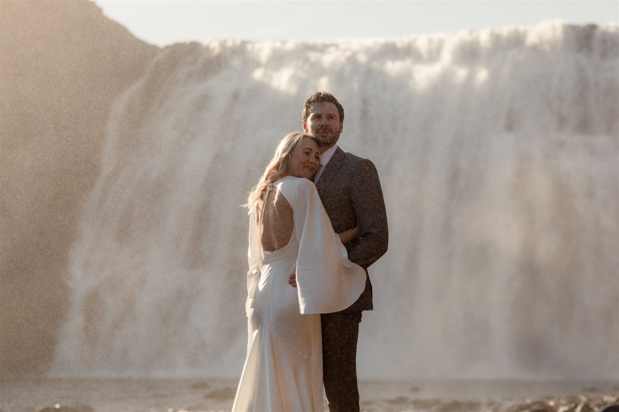 Lord of the Rings Inspired Iceland Engagement Photoshoot at waterfall — couple standing together with Arwen inspired dress with beautiful light and waterfall mist