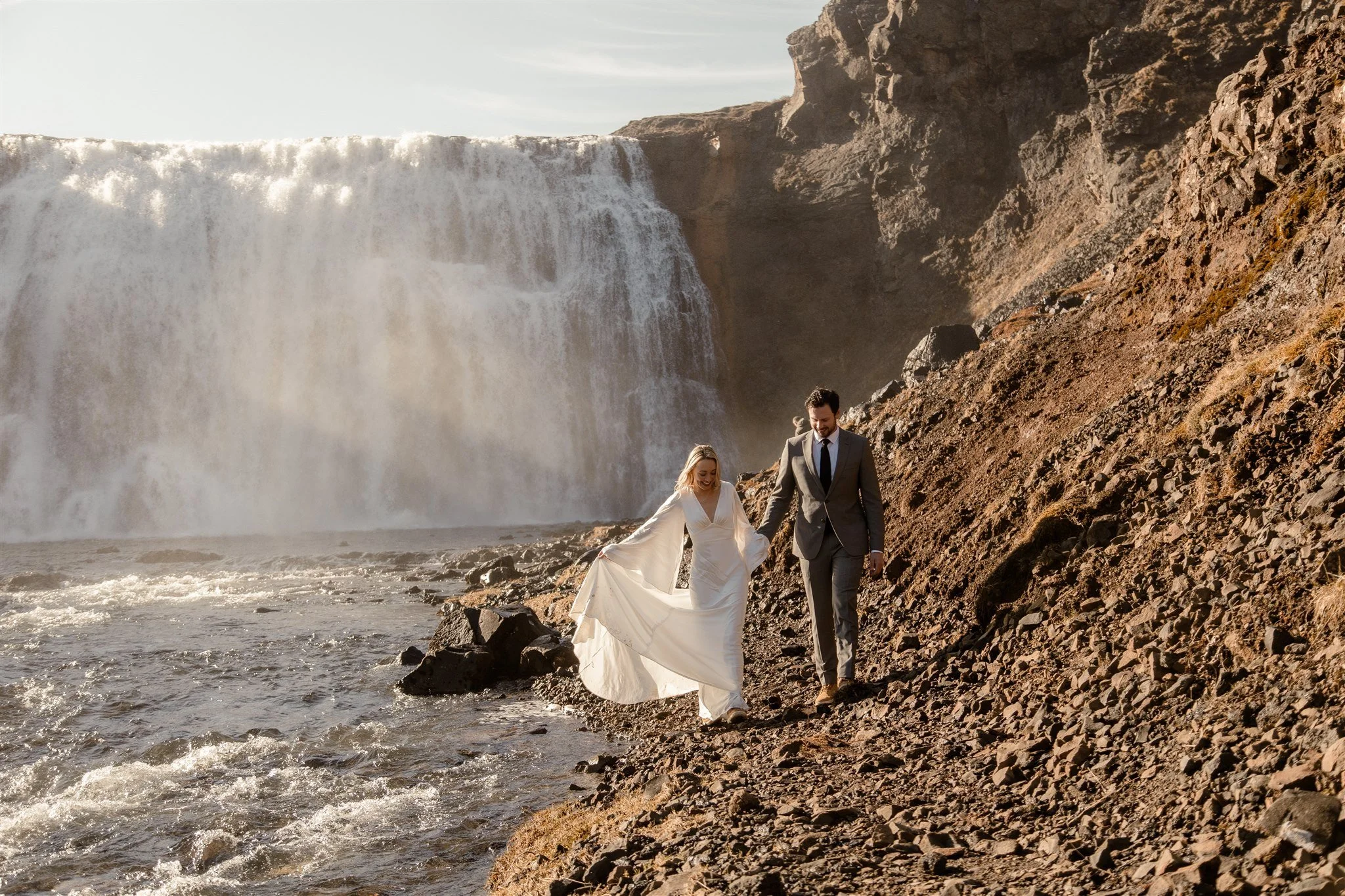 Lord of the Rings Inspired Iceland Engagement Photoshoot at waterfall — couple standing together with Arwen inspired dress with beautiful light and waterfall mist