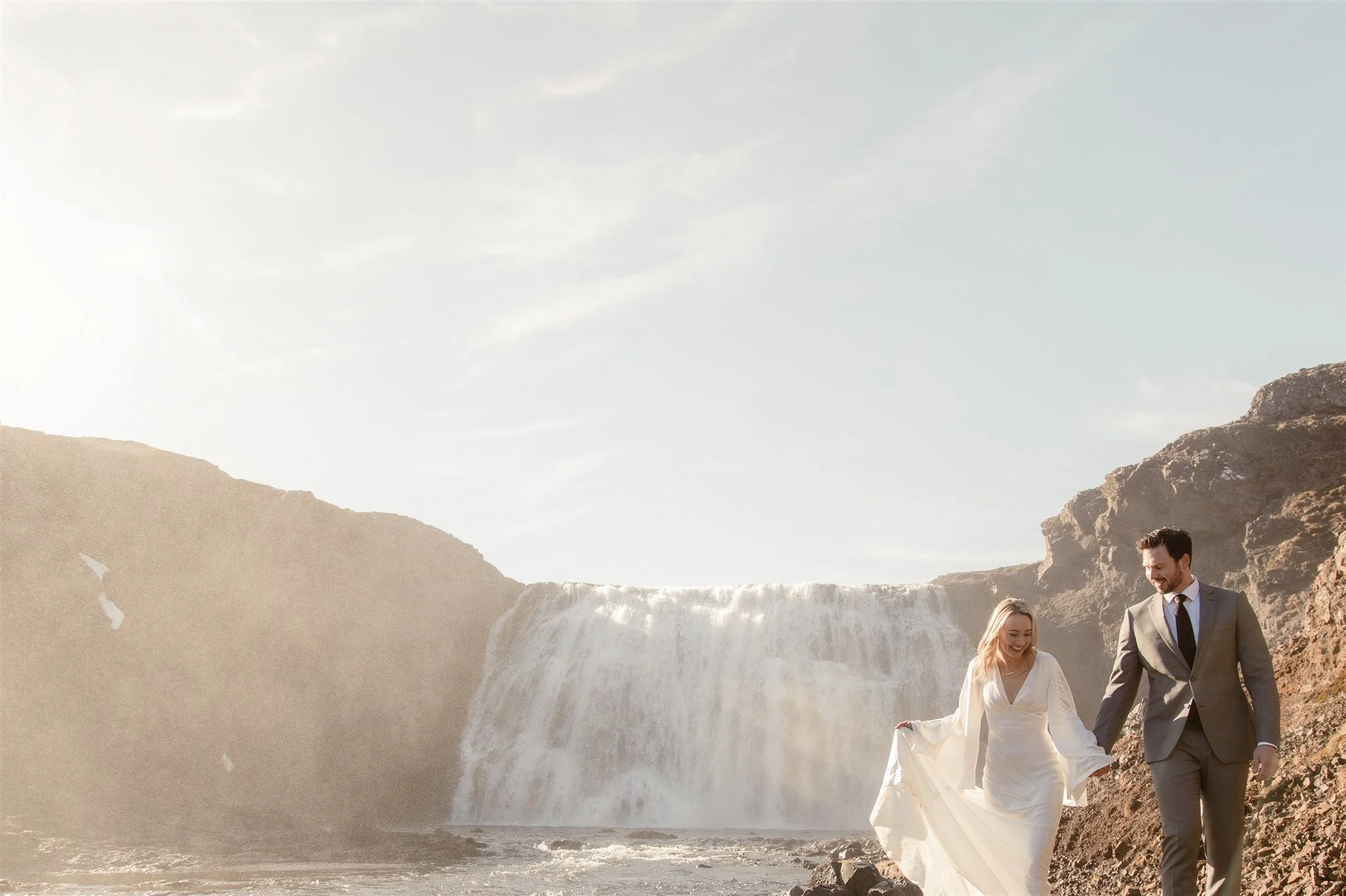 Lord of the Rings Inspired Iceland Engagement Photoshoot at waterfall — couple standing together with Arwen inspired dress with beautiful light and waterfall mist