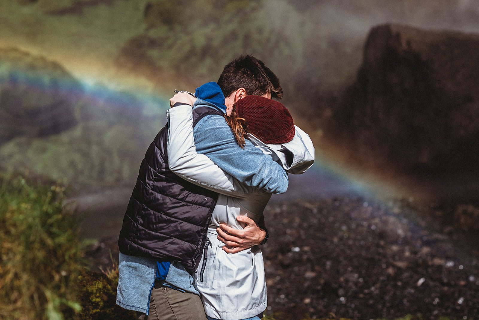couple after their Iceland proposal hugging to celebrate under a rainbow at a private waterfall