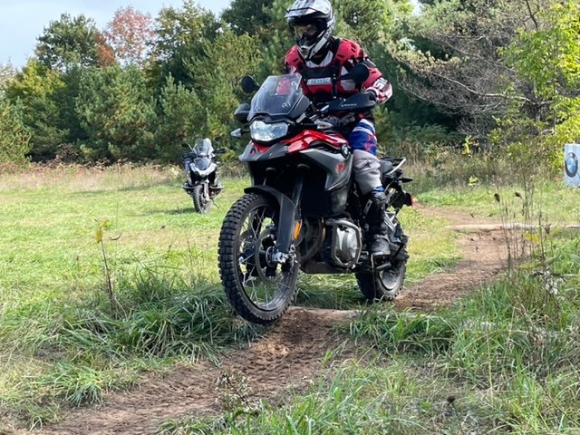 Motorcycle riding over log on dirt trail.