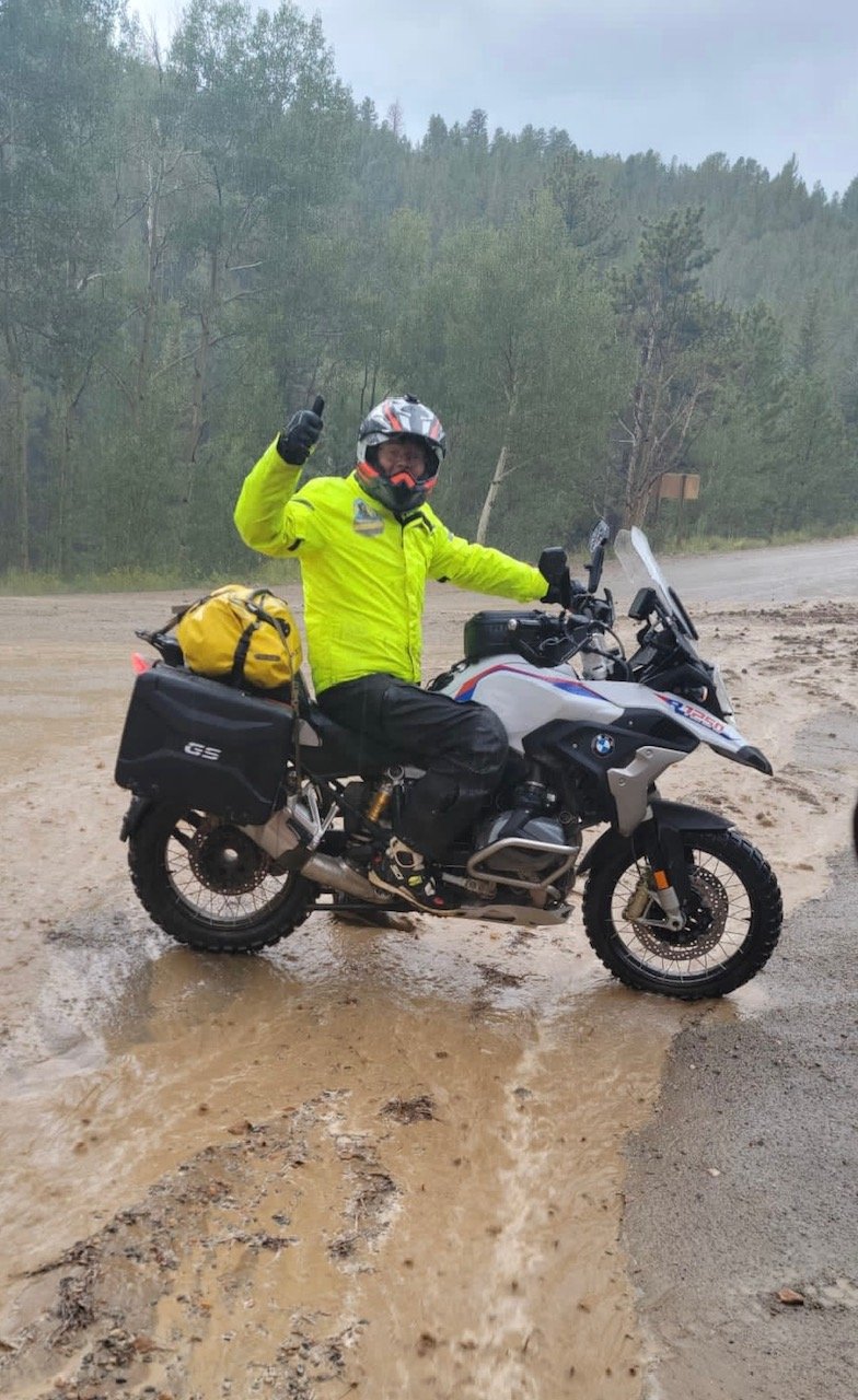  Motorcycle rider waving on motorcycle loaded with gear in rain.   