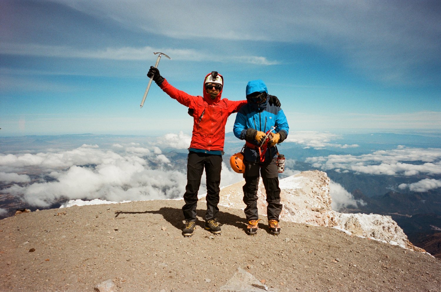  Two men in climbing gear at summit of mountain. 