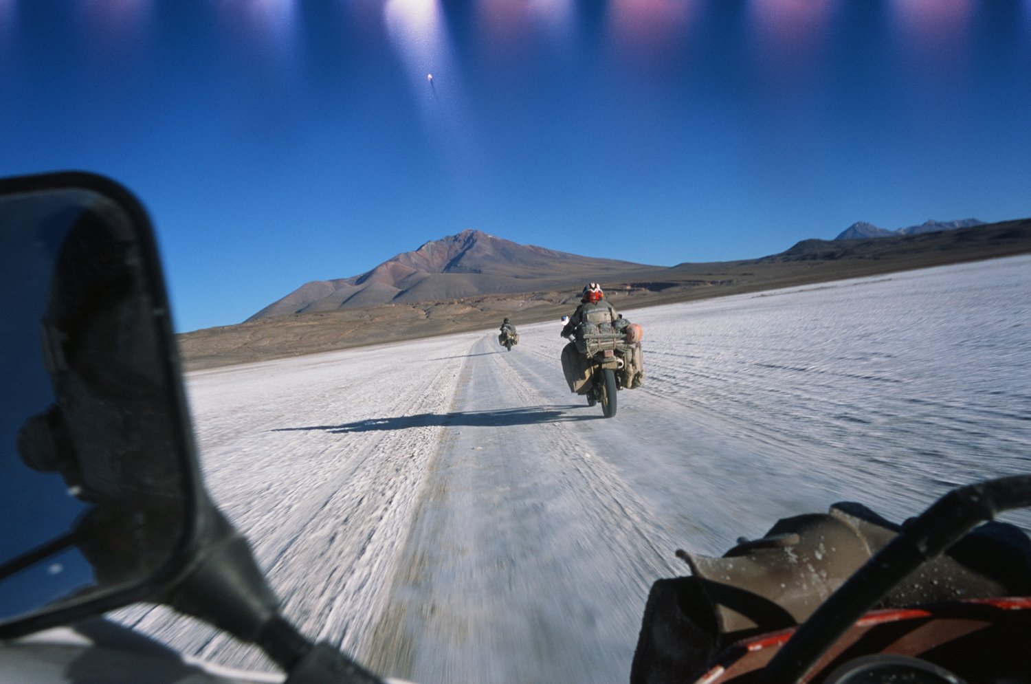  POV from motorcycle - two motorcycles ahead on snow covered and icy road headed towards a mountain. 