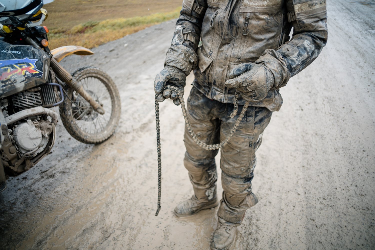  Motorcycle and mud covered rider with broke motorcycle chain in his hands. 