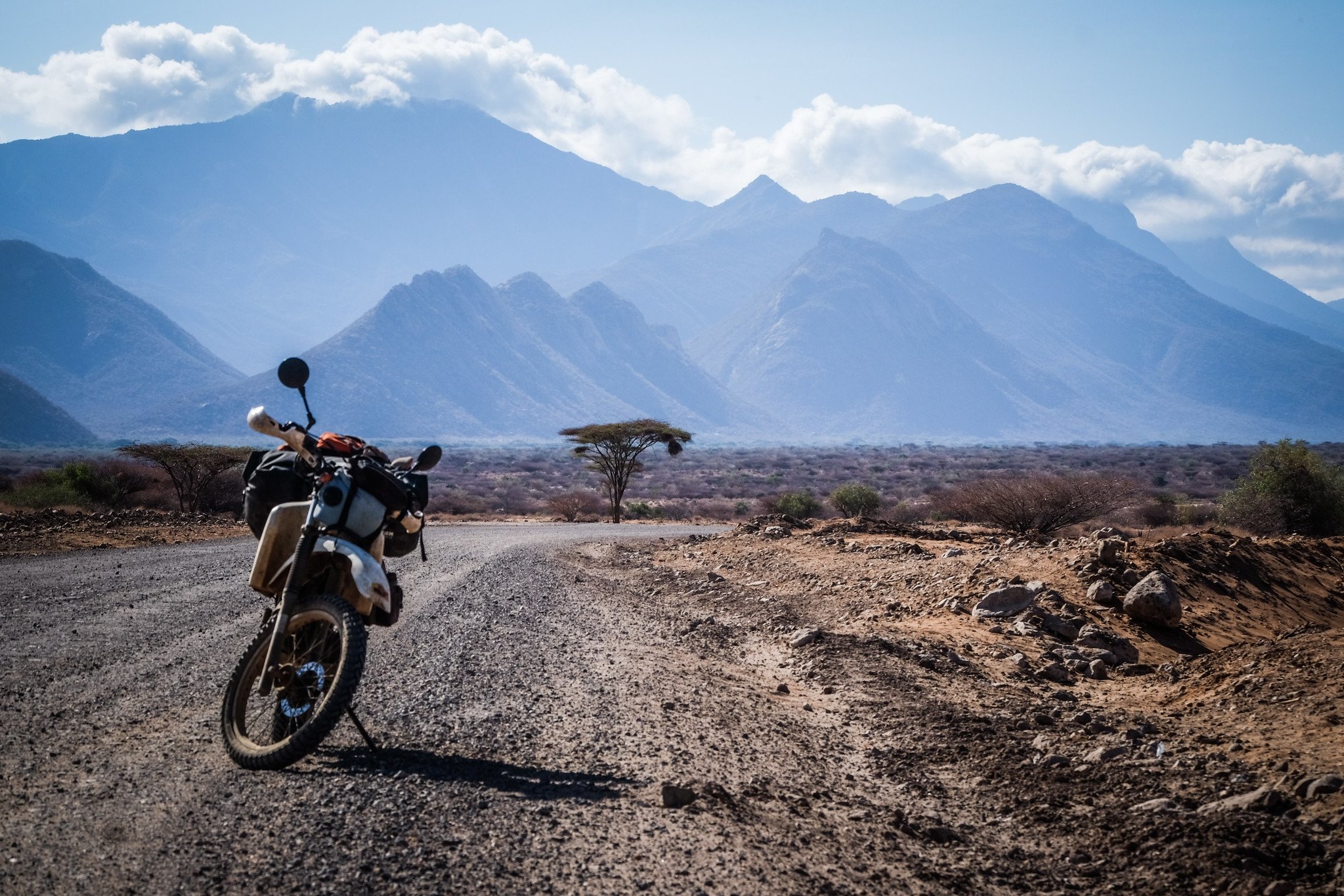  Motorcycle parked on gravel road with mountains in background. 