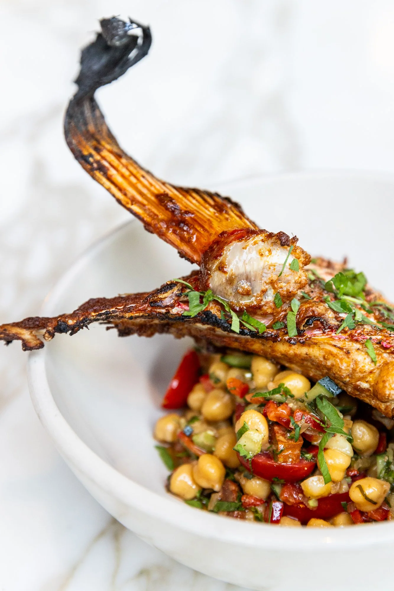 Close-up of grilled lamb chop resting on a chickpea salad with herbs in a white bowl. Ovenbird Restaurant in Birmingham, Alabama.