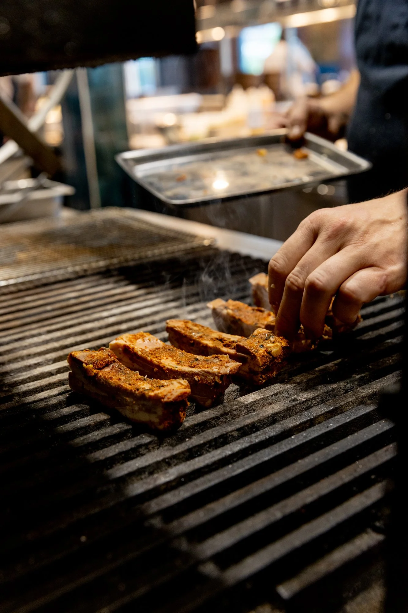 Chef placing racks of seasoned ribs on a grill in a kitchen or restaurant setting.