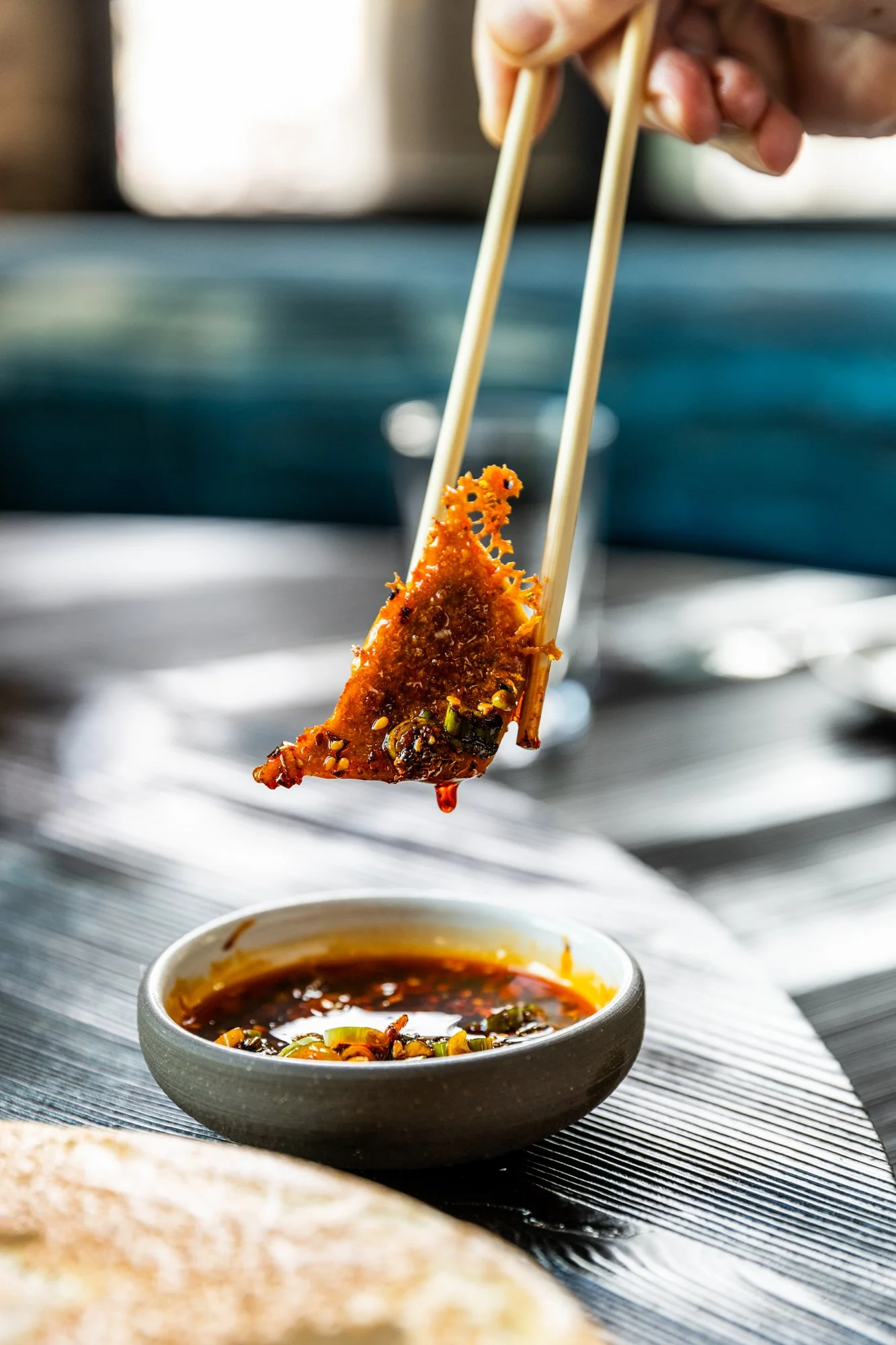 A hand using chopsticks to hold a piece of fried dumpling dipped in soy sauce.