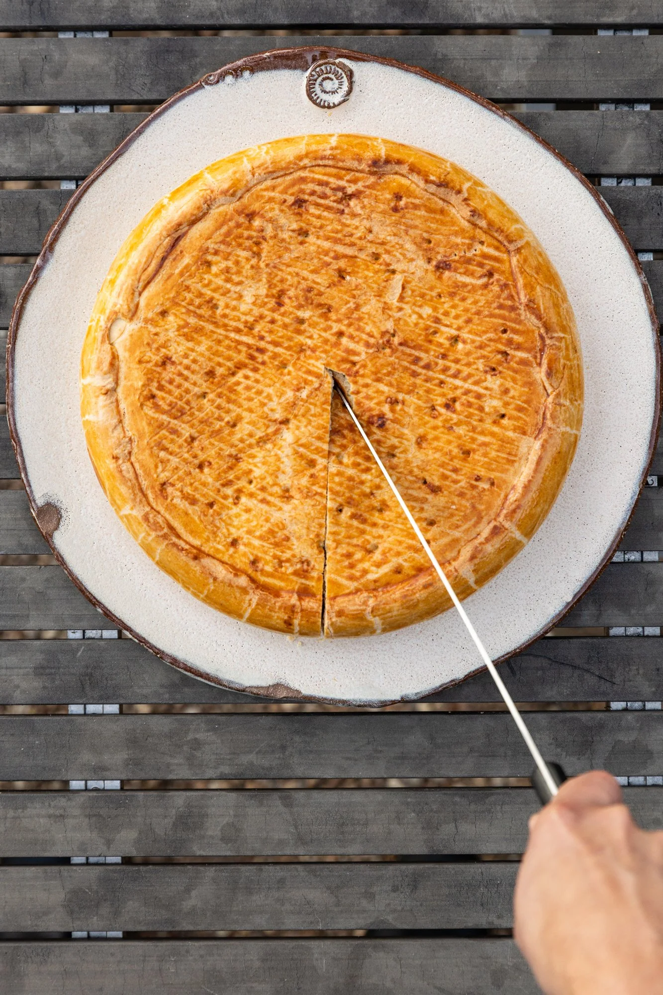 A person is cutting a large Apple Pie with a chef knife on a round wooden board. Ovenbird Restaurant in Birmingham, Alabama.