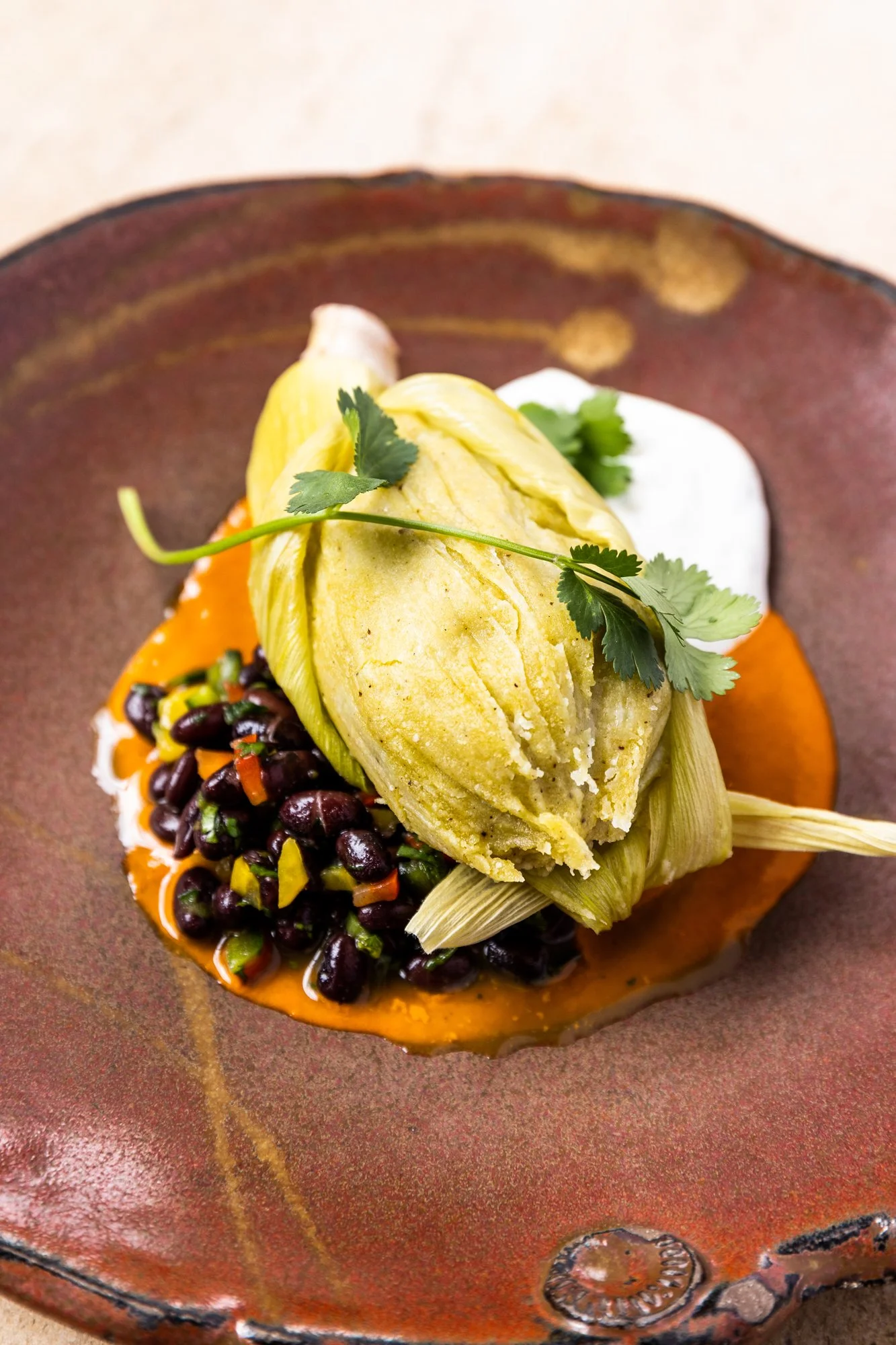 A serving of Mexican street corn, black beans salad, and avocado on a dark ceramic plate. Hot and Hot Fish Club Restaurant in Birmingham, Alabama.