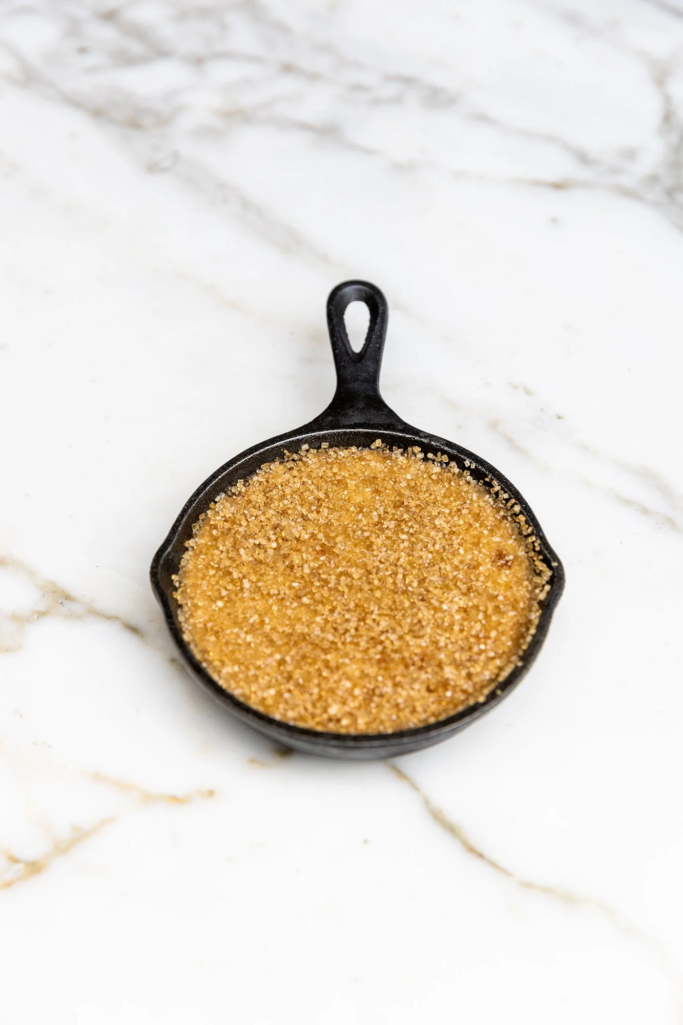 A small cast iron skillet filled with brown sugar on a white marble countertop. Ovenbird Restaurant in Birmingham, Alabama.