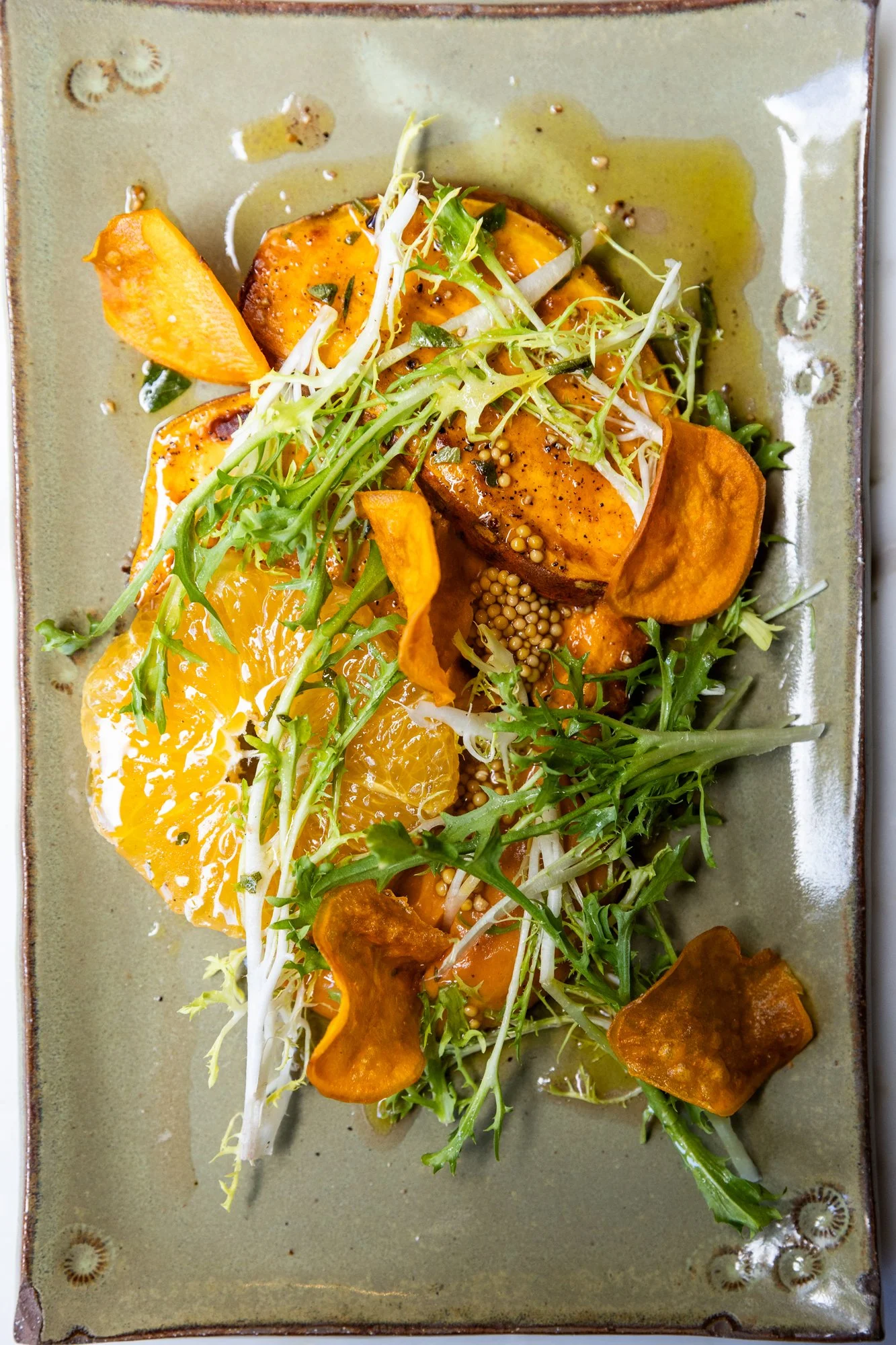 A plated salad with orange slices, roasted sweet potatoes, fresh greens, and mustard seeds, drizzled with a light dressing. Ovenbird Restaurant in Birmingham, Alabama.