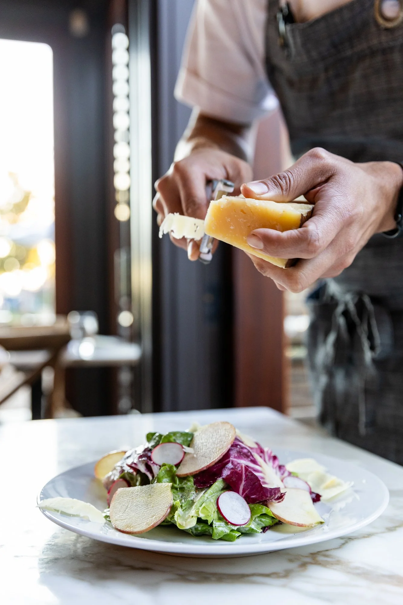 Person grating cheese over a salad at a restaurant Ovenbird Restaurant in Birmingham, Alabama.