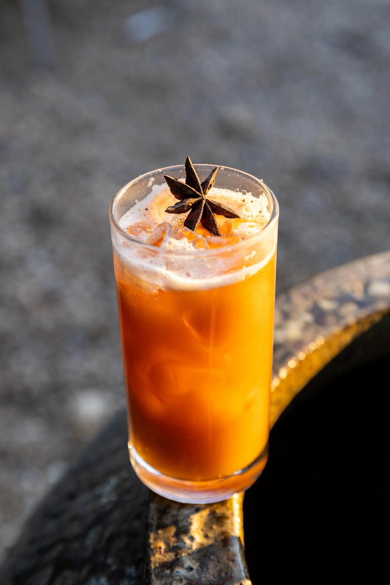A tall glass of orange-colored iced beverage garnished with a star anise spice. Ovenbird Restaurant in Birmingham, Alabama.