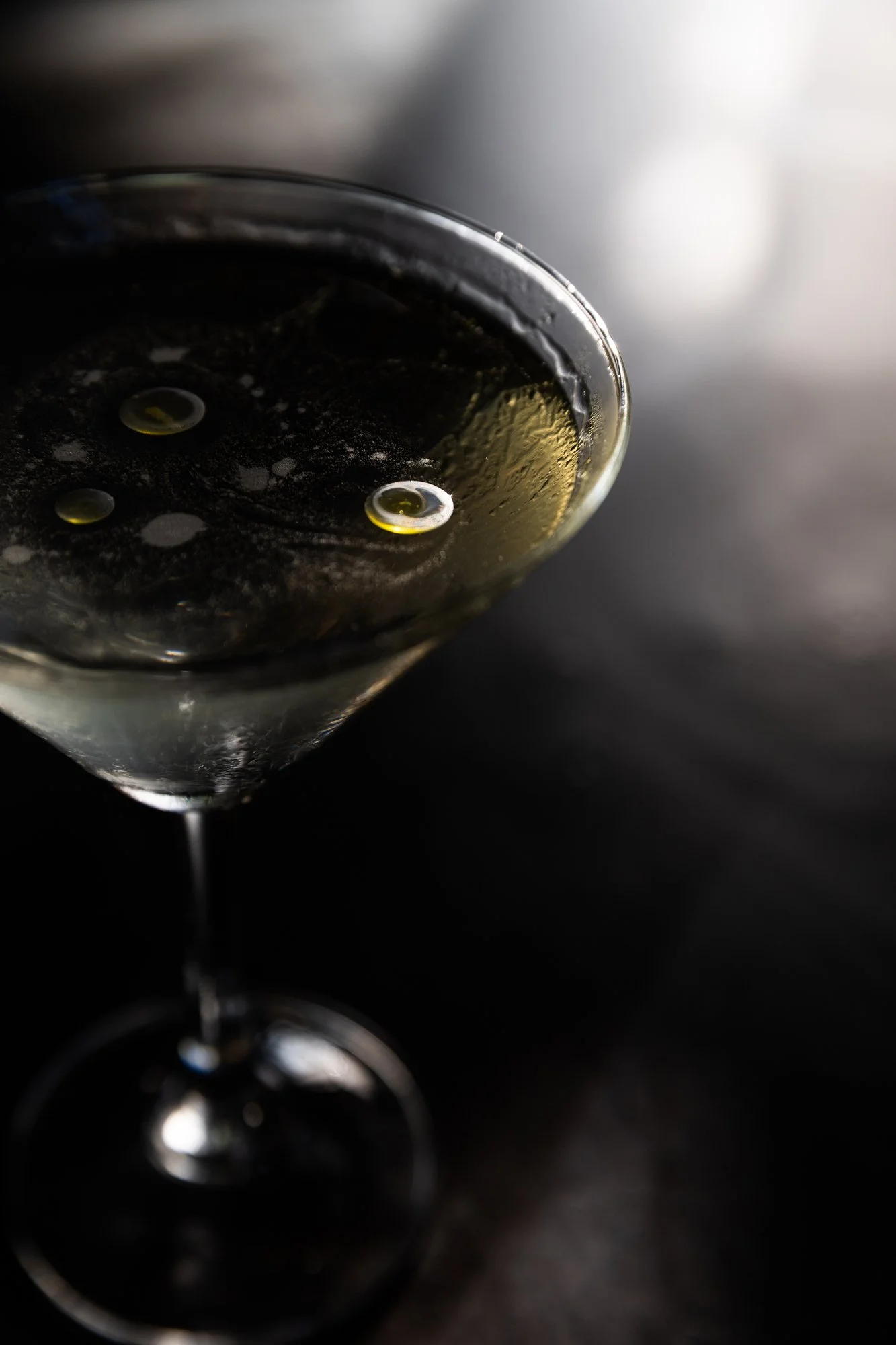 Close-up of a glass of dark-colored beverage with a few bubbles, set against a dark background.
