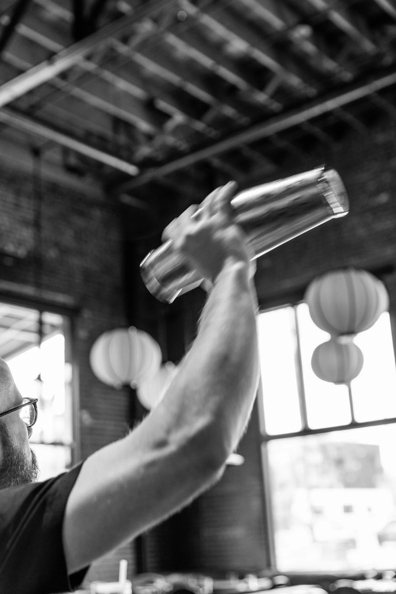 A person with a beard and glasses holding a clear glass bottle upside down.