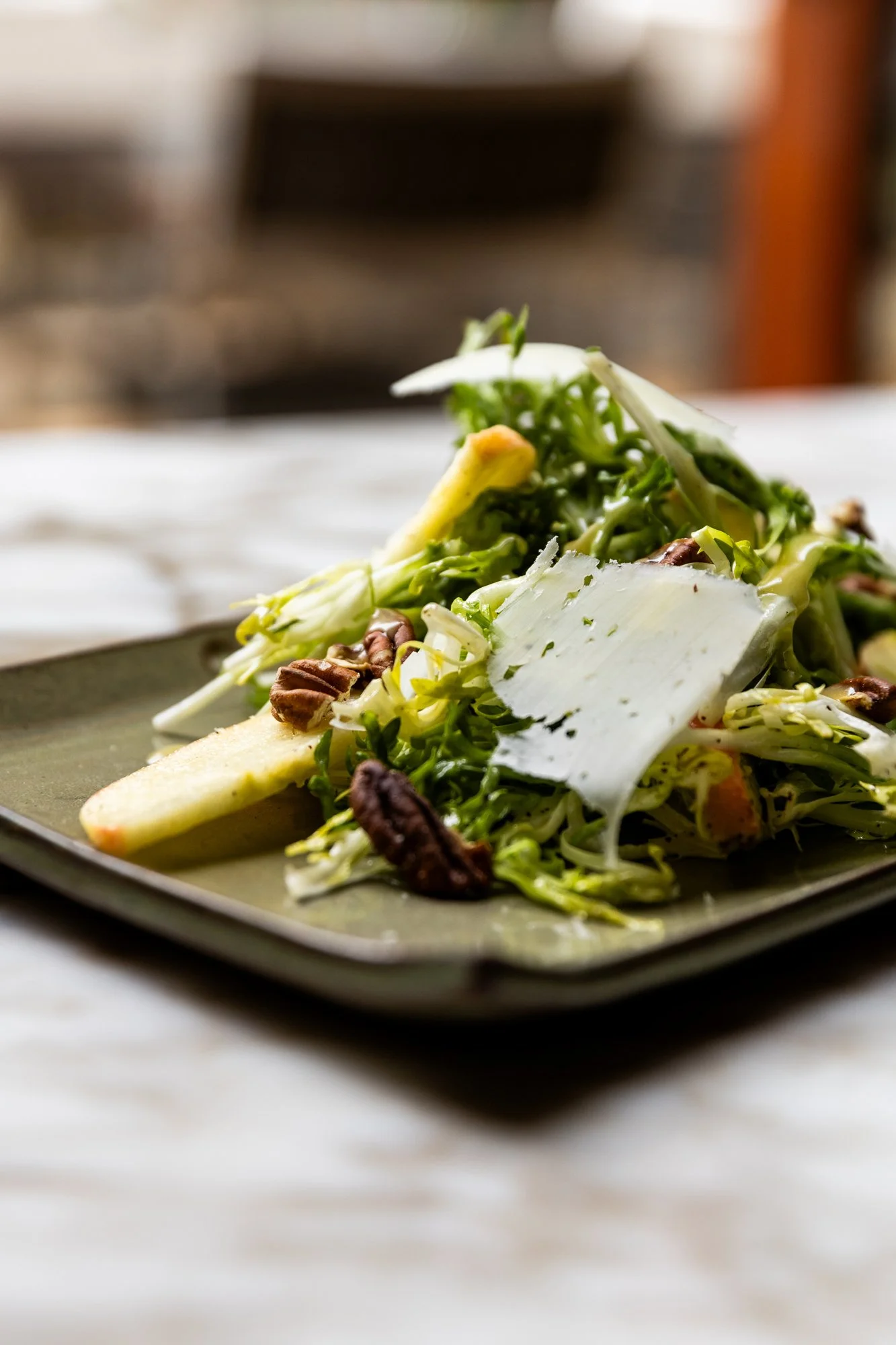Close-up of a fresh green salad with sliced pears, walnuts, and shaved cheese on a green plate. Ovenbird Restaurant in Birmingham, Alabama.