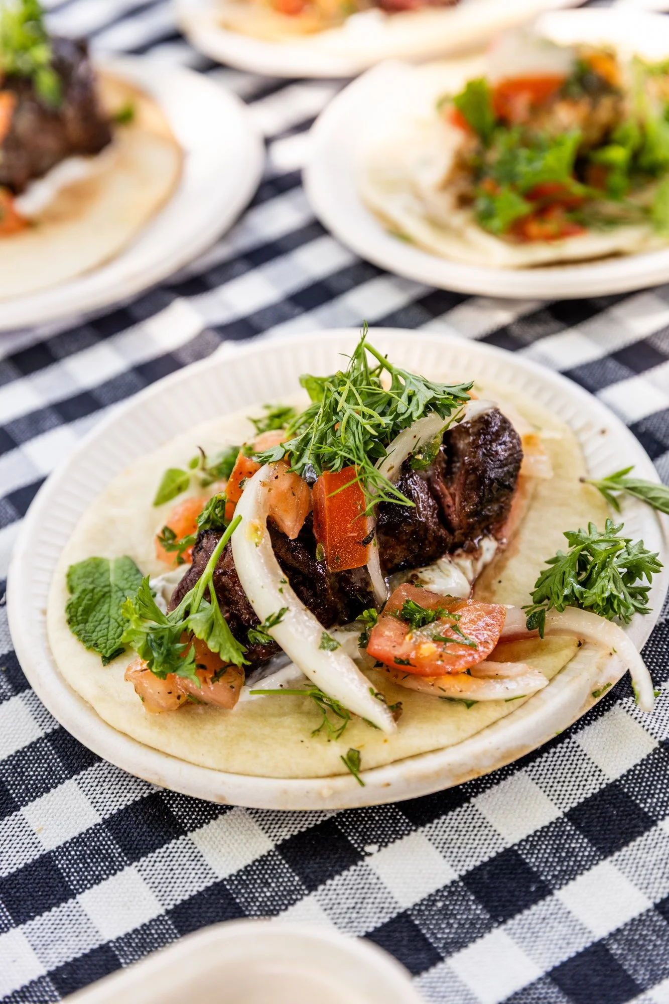 A taco filled with beef, fresh herbs, tomatoes, and onions on a paper plate, sitting on a black and white checkered tablecloth with two other tacos in the background. Southbound Food Festival in Birmingham, Alabama.