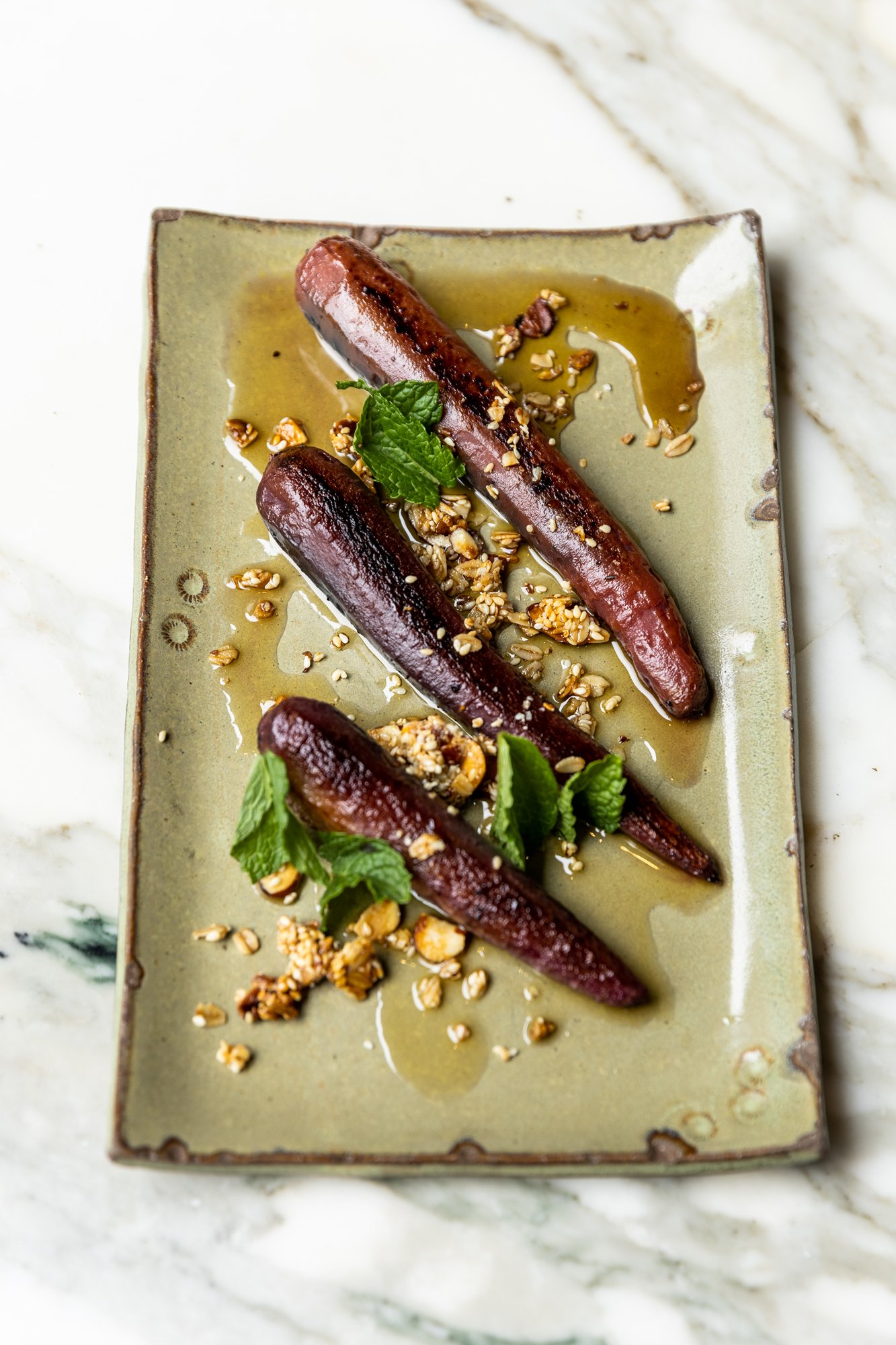 Roasted carrots garnished with herbs and crushed nuts, drizzled with honey or syrup, served on a rectangular ceramic plate. Ovenbird Restaurant in Birmingham, Alabama.