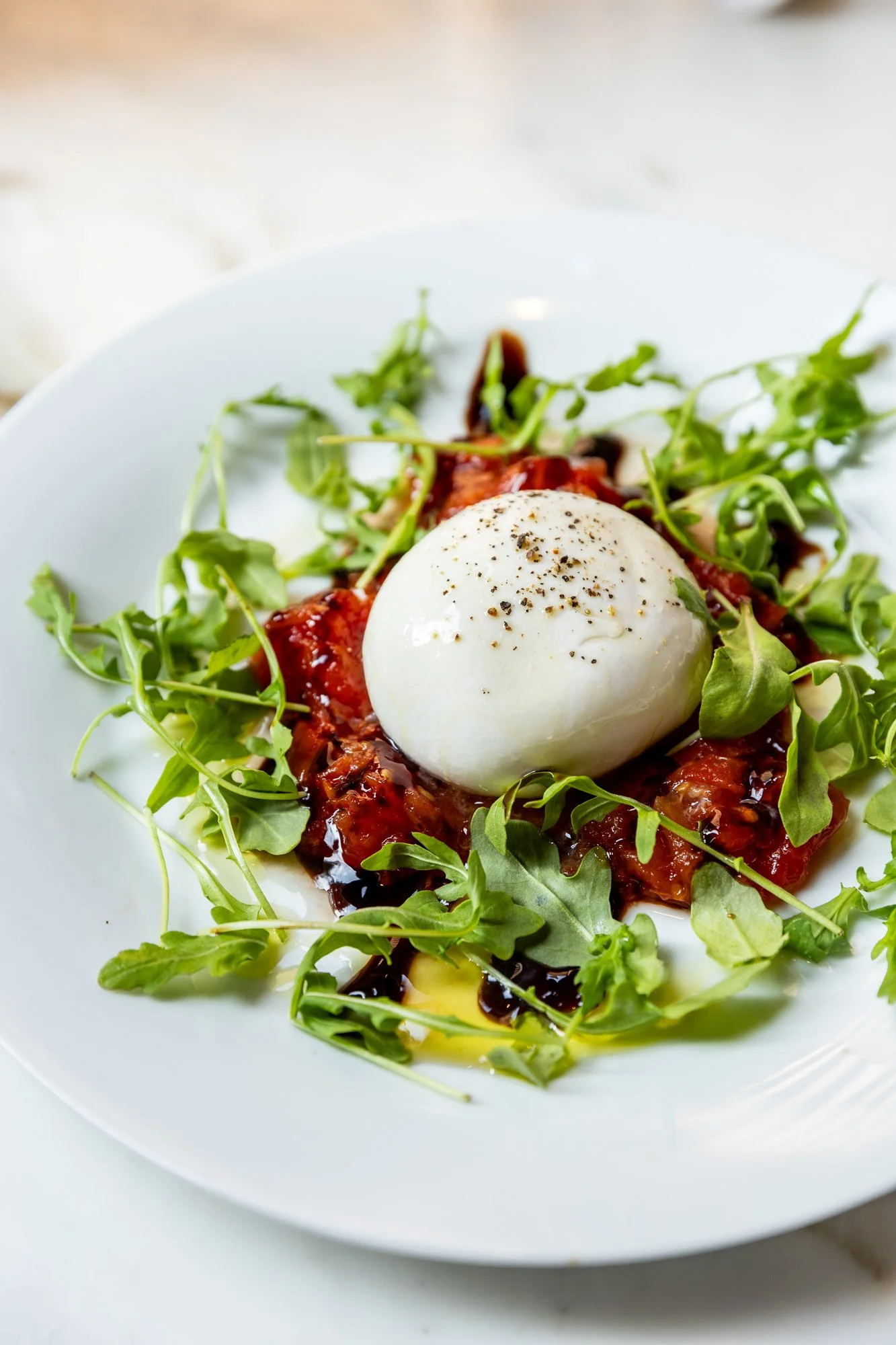 Poached egg on tomato salad with arugula and balsamic glaze Ovenbird Restaurant in Birmingham, Alabama.