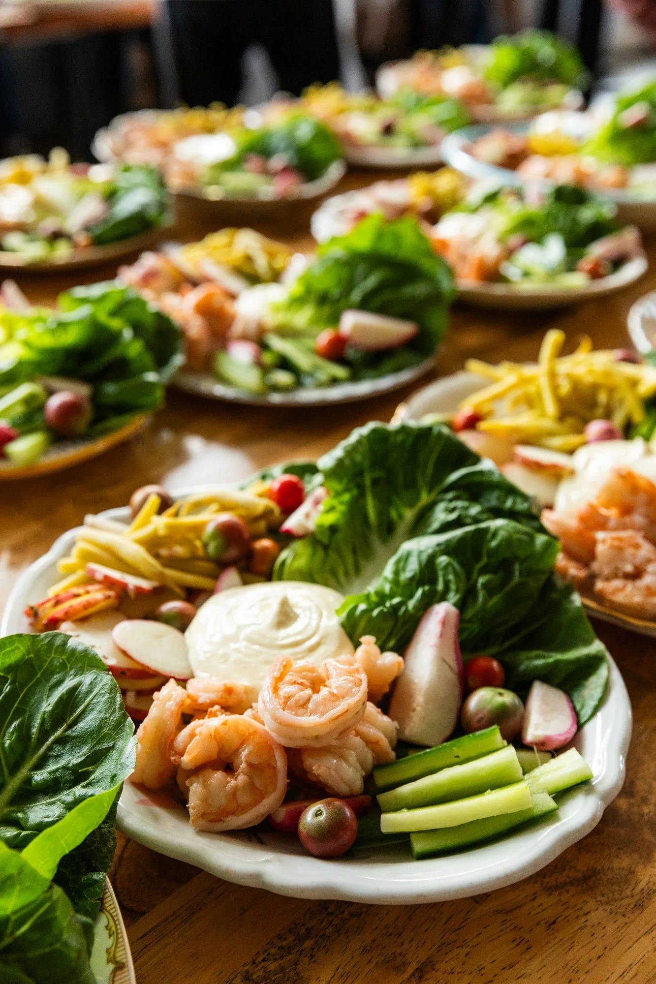 Several plates of shrimp, lettuce, radishes, cucumber, and other vegetables, with some plates featuring shredded cheese and slices of boiled eggs, arranged on a wooden table. Southbound Food Festival in Birmingham, Alabama.
