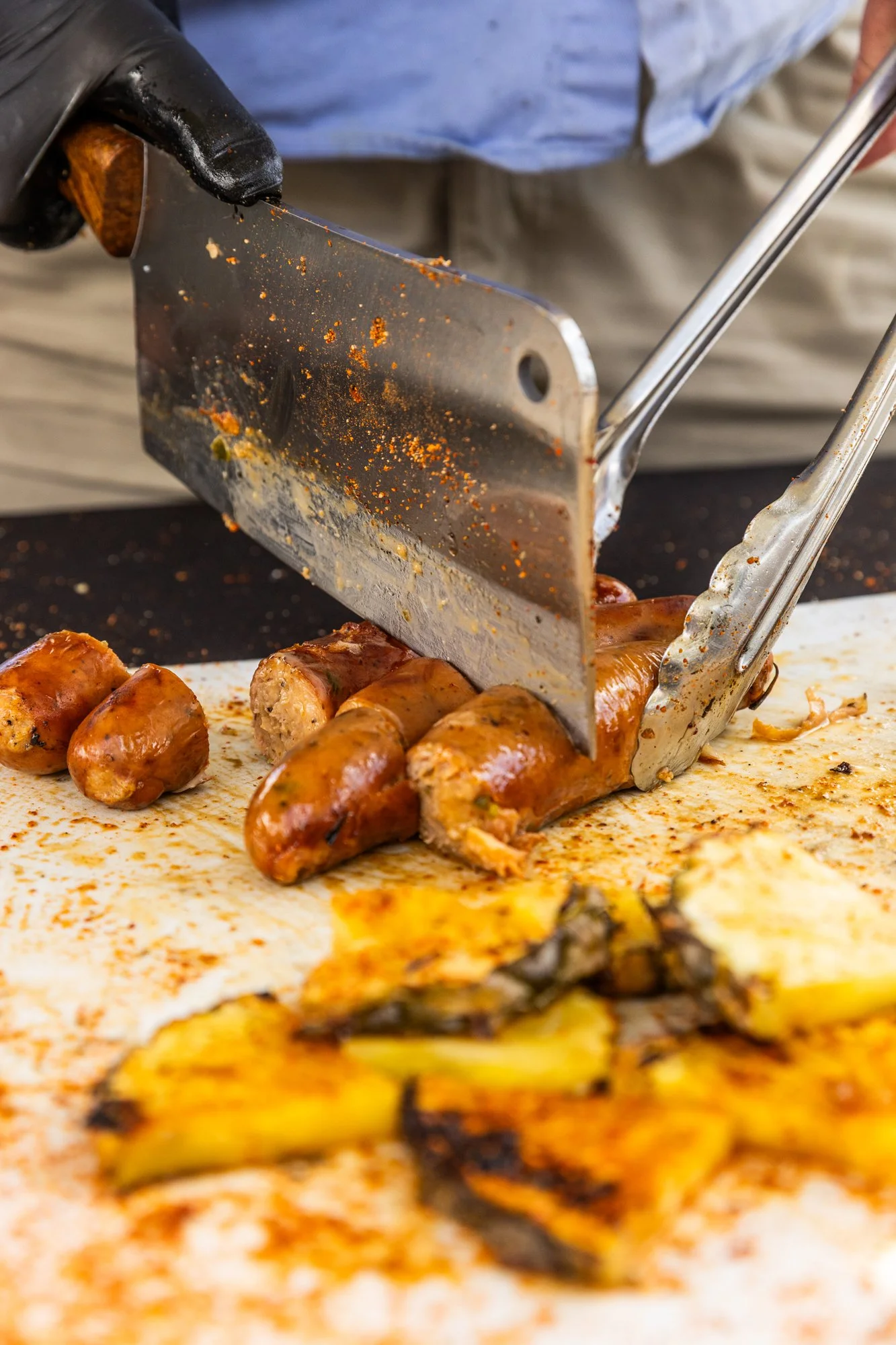 A person slices cooked sausages on a cutting board with tongs, with grilled vegetables in the foreground. Southbound Food Festival in Birmingham, Alabama.