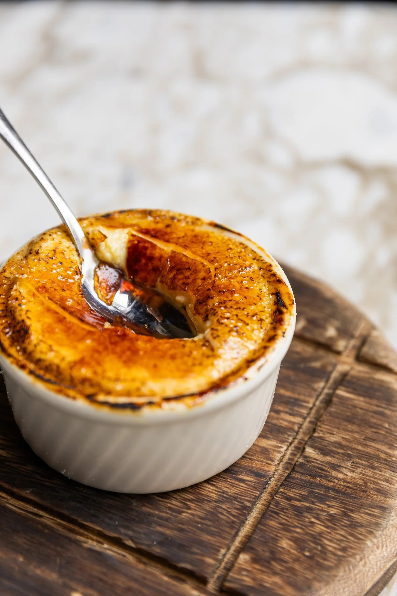 A ramekin of caramelized bananas foster with a spoon, placed on a wooden serving board. Ovenbird Restaurant in Birmingham, Alabama.