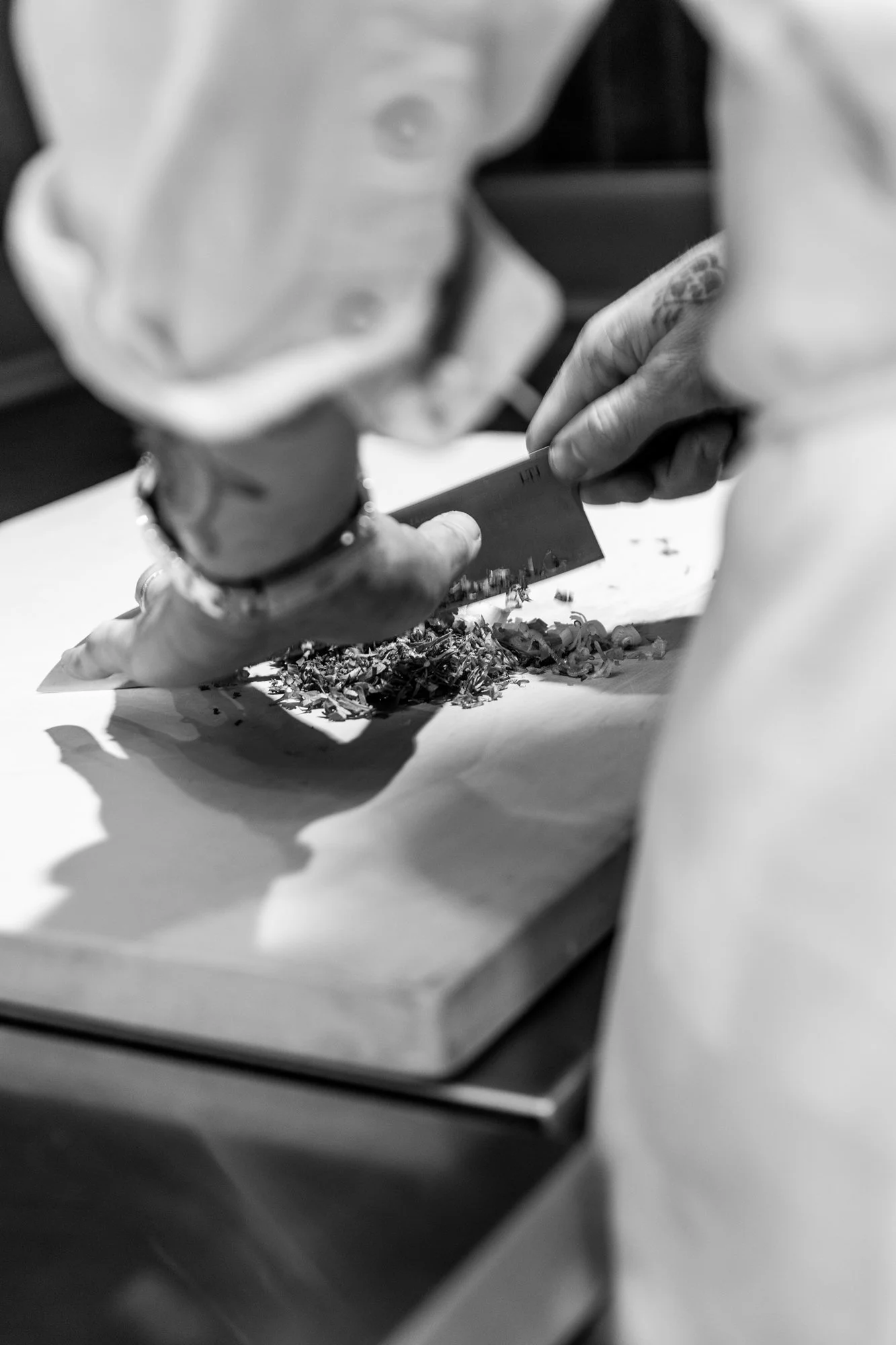 Person chopping herbs or vegetables on a cutting board with a knife.