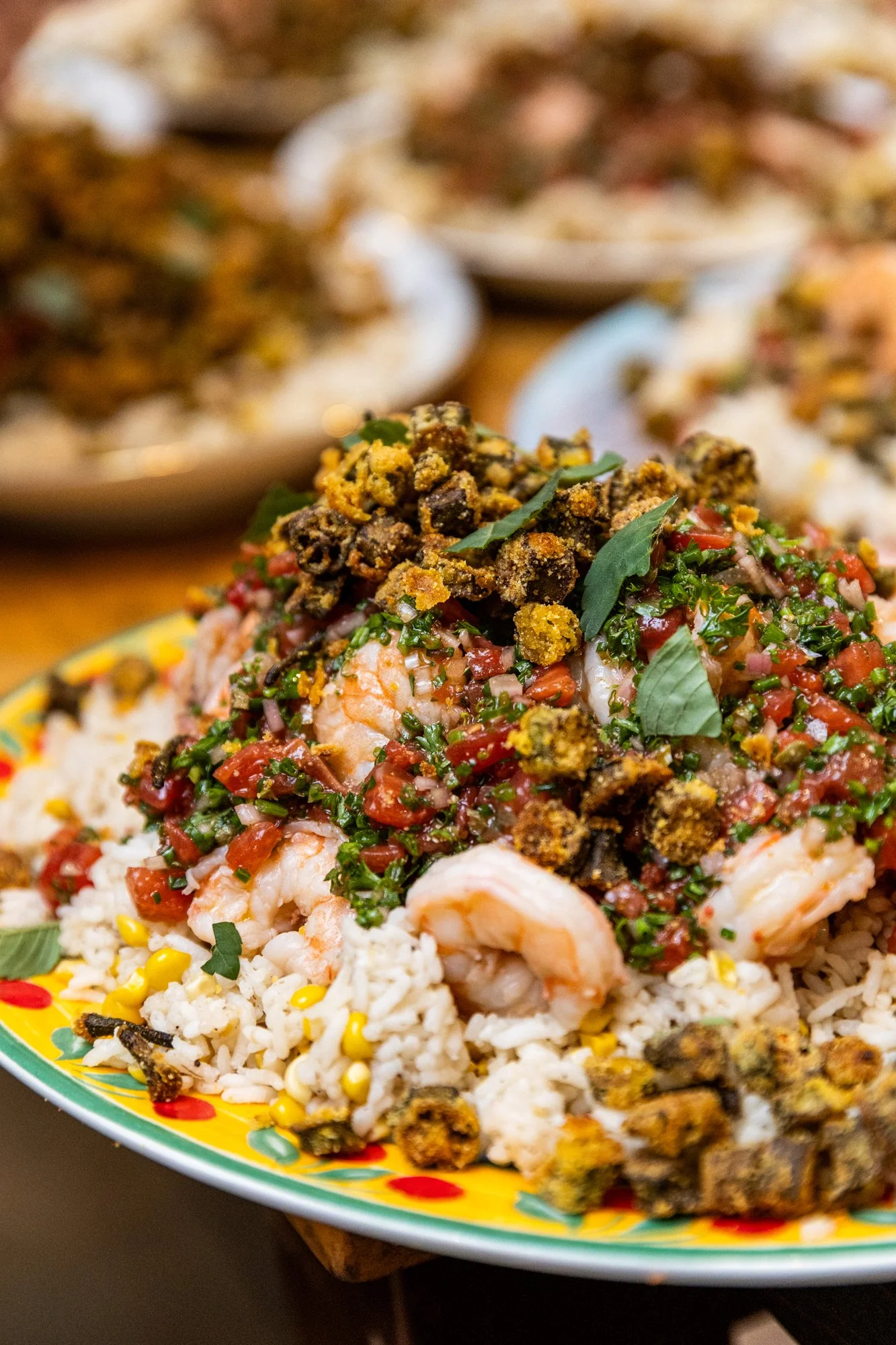 A dish of rice topped with shrimp, chopped tomatoes, herbs, and crispy fried crumbles, served on a colorful plate. Southbound Food Festival in Birmingham, Alabama.