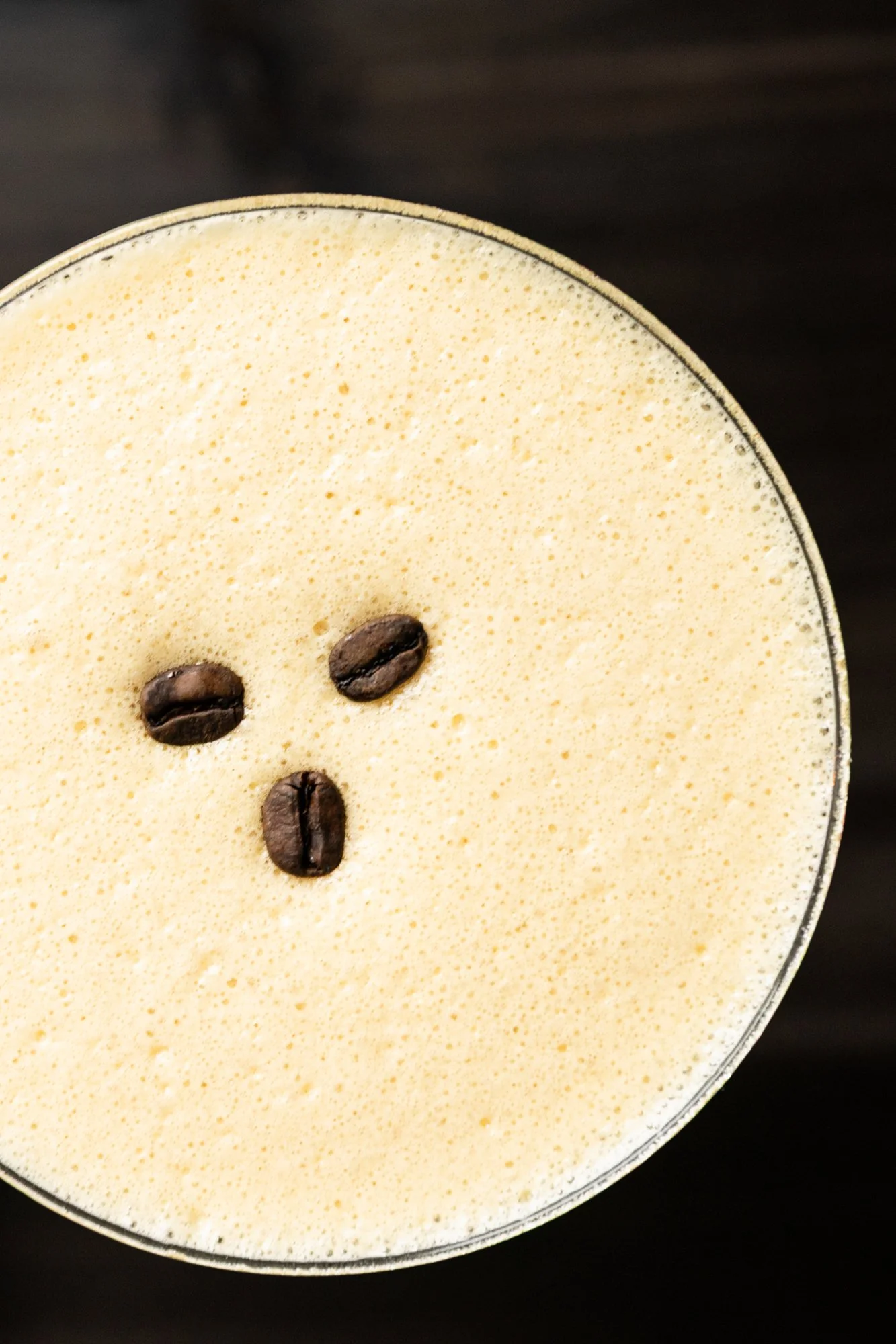 Close-up of a frothy coffee drink topped with three coffee beans arranged to resemble a face.