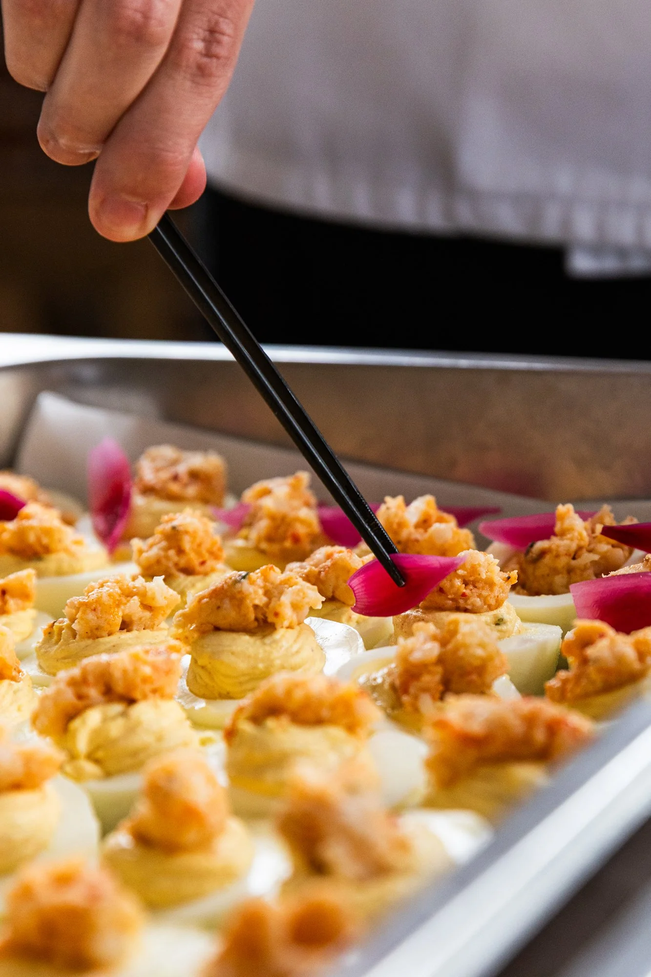 Person using chopsticks to garnish or serve mini appetizers topped with crab meat and pink flower petals on a tray. Southbound Food Festival in Birmingham, Alabama.