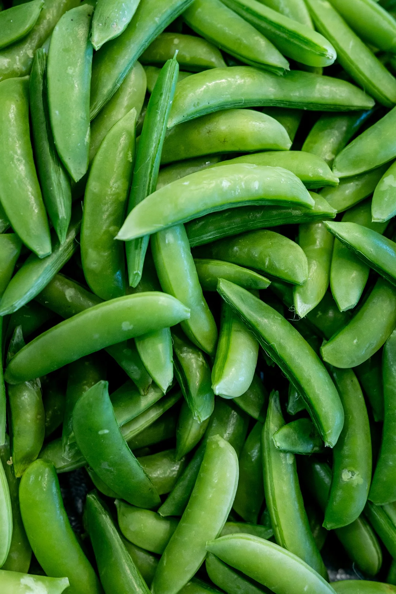 Close-up of fresh green snap peas with some pods slightly open, showing the peas inside.