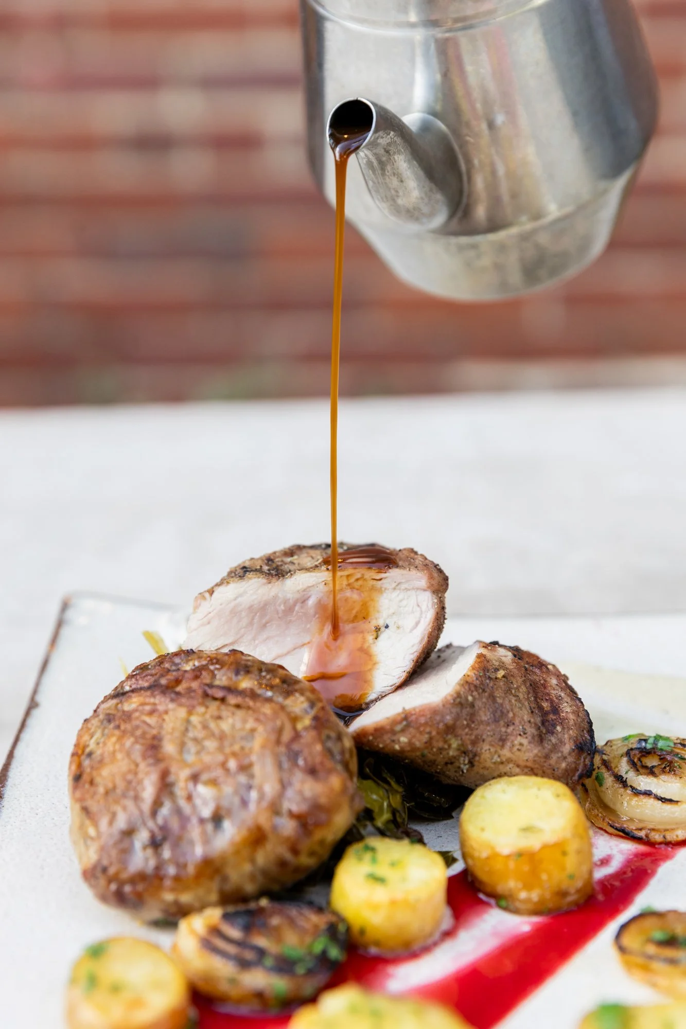 A plate of grilled chicken, roasted vegetables, and a bowl, with gravy being poured from a metal gravy boat over the chicken. Hot and Hot Fish Club Restaurant in Birmingham, Alabama.