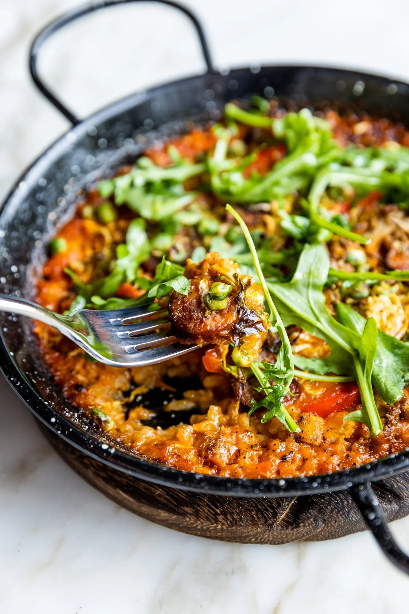 A close-up of a skillet with a serving of cheesy baked dish topped with fresh arugula and greens. Ovenbird Restaurant in Birmingham, Alabama.