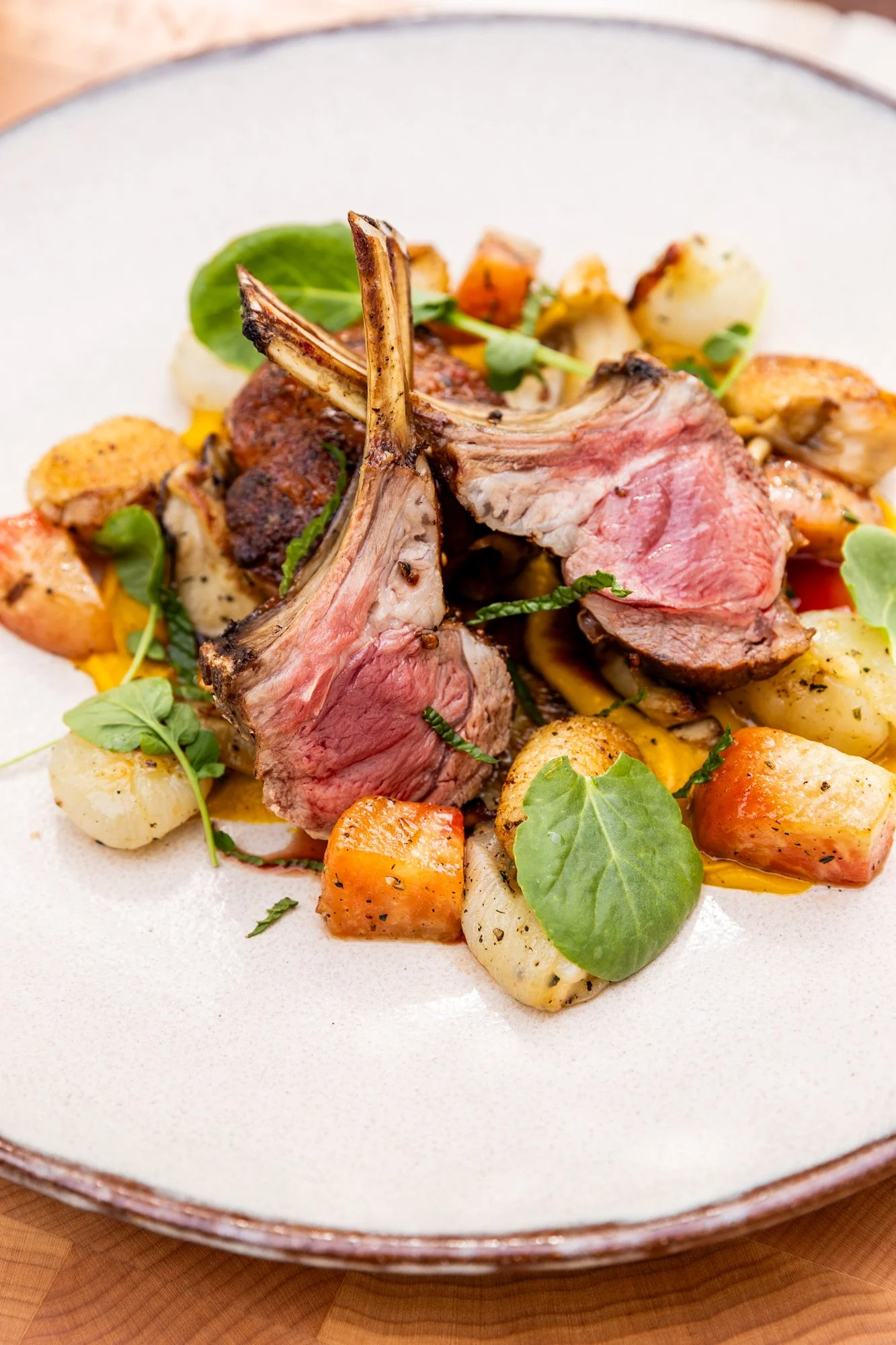 Rack of lamb with roasted vegetables and fresh herbs on a white plate. Hot and Hot Fish Club Restaurant in Birmingham, Alabama.