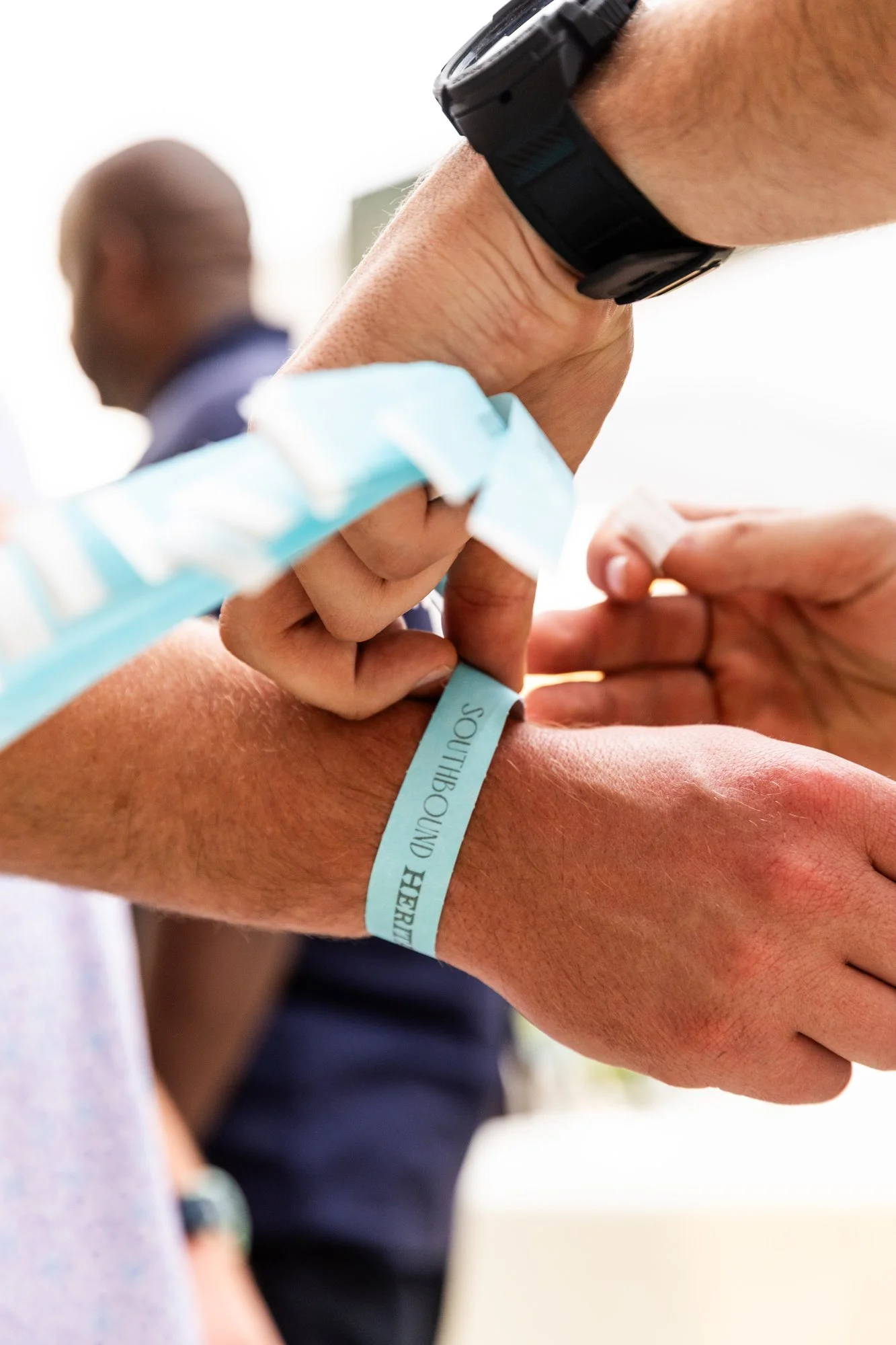 Person putting a hospital wristband on their wrist, with another person assisting, in a medical setting. Southbound Food Festival in Birmingham, Alabama.