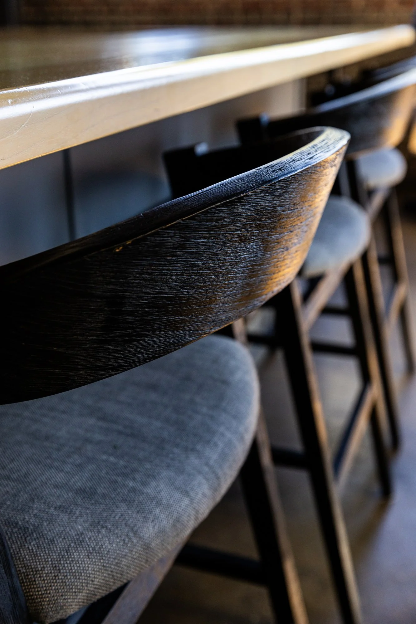 Close-up of bar stools with cushioned seats and wooden backs at a bar or counter. Hot and Hot Fish Club Restaurant in Birmingham, Alabama.