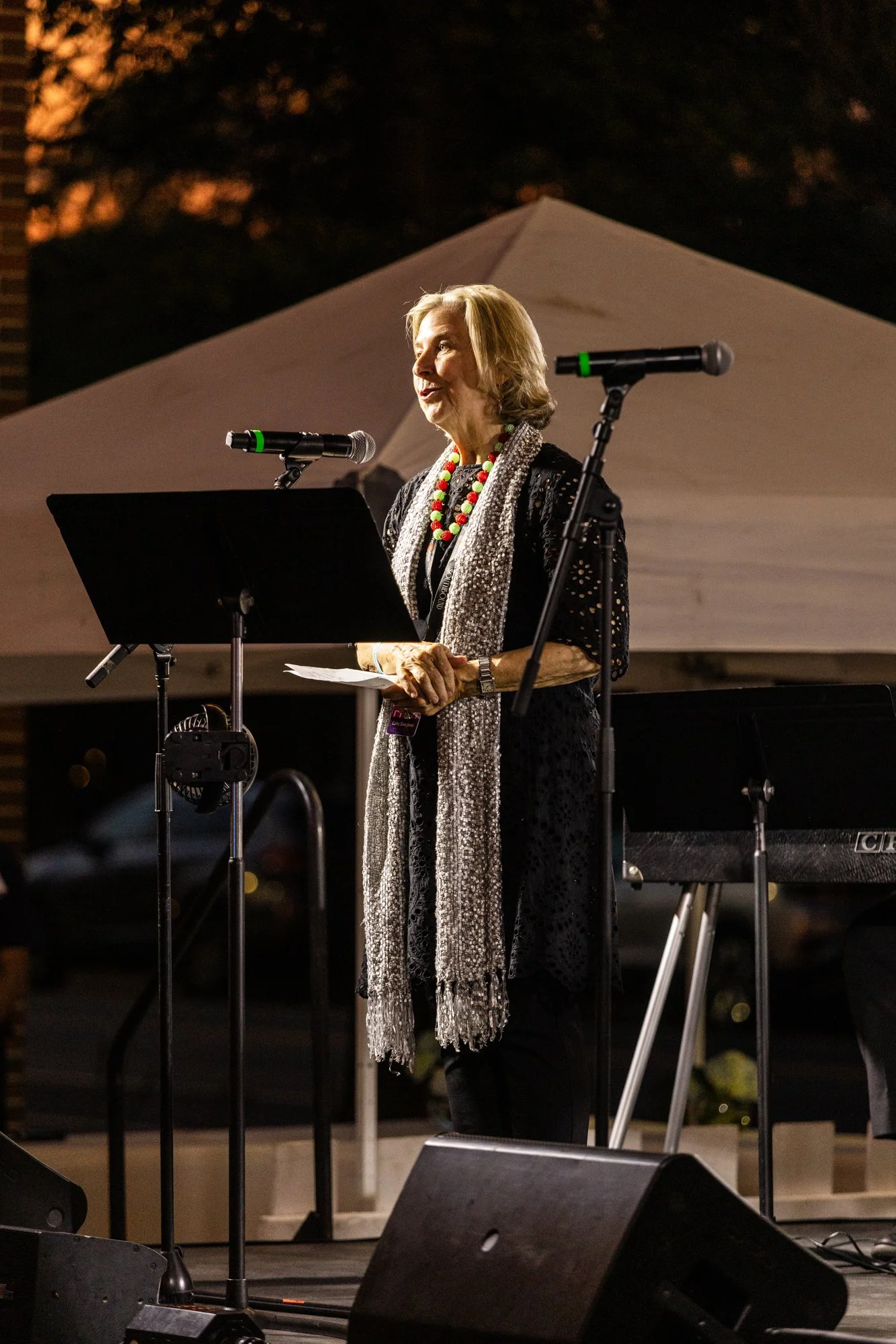 An elderly woman speaking at an outdoor event during the evening, standing behind a music stand and two microphones, with a tent in the background. Southbound Food Festival in Birmingham, Alabama.