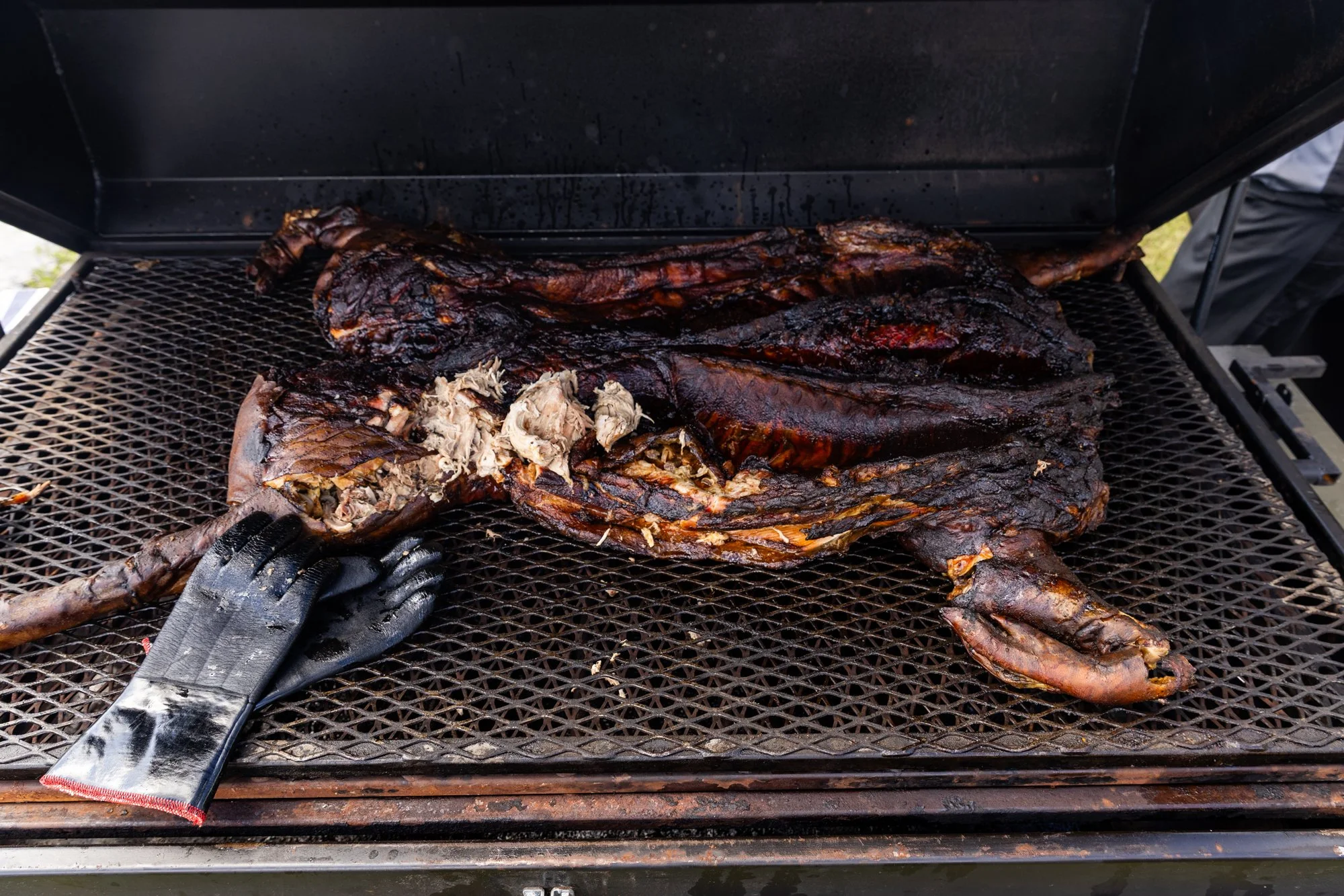 Whole smoked or grilled fish with some of its meat exposed, on a metal grill surface, with a gloved hand pulling at the meat. Southbound Food Festival in Birmingham, Alabama.