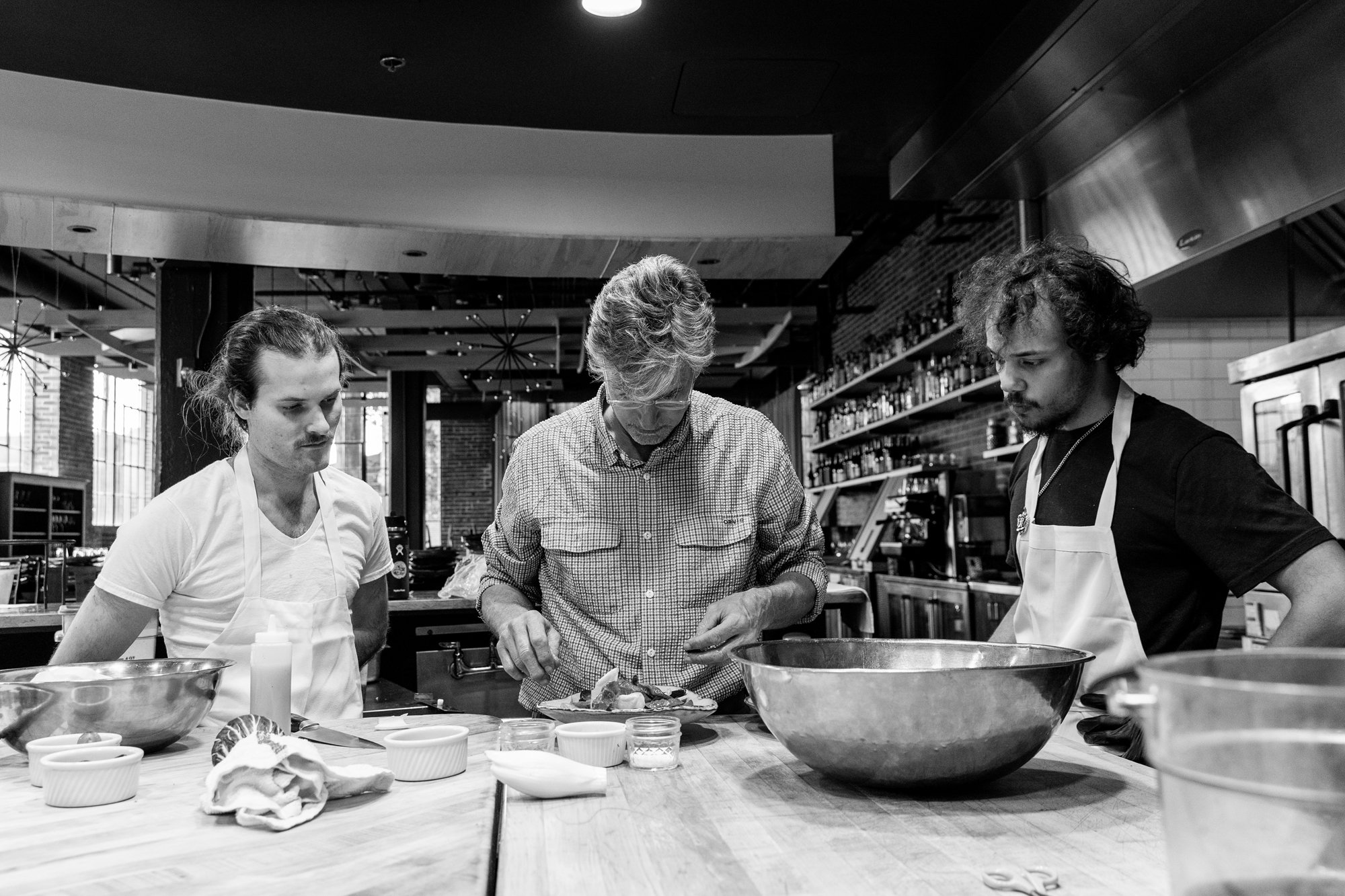 Three men in a kitchen preparing food, with various bowls and ingredients on the counter. Hot andHot Fish Club Restaurant in Birmingham, Alabama.
